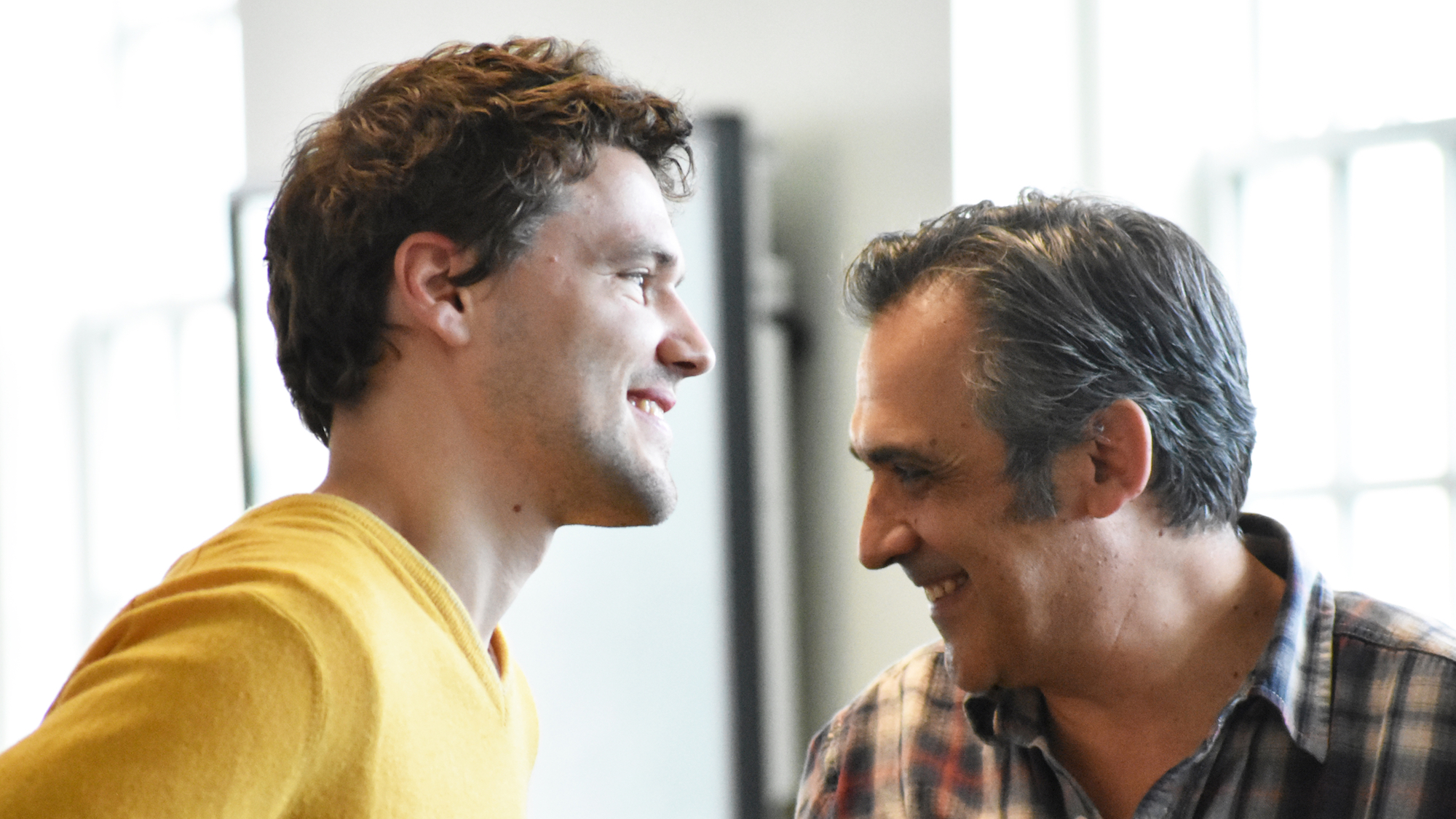 Aaron Doliana, a PhD student in Linguistics, looking to the right in the foreground and smiling, as Professor Juan Uriagereka looks to the left and smiles in the background
