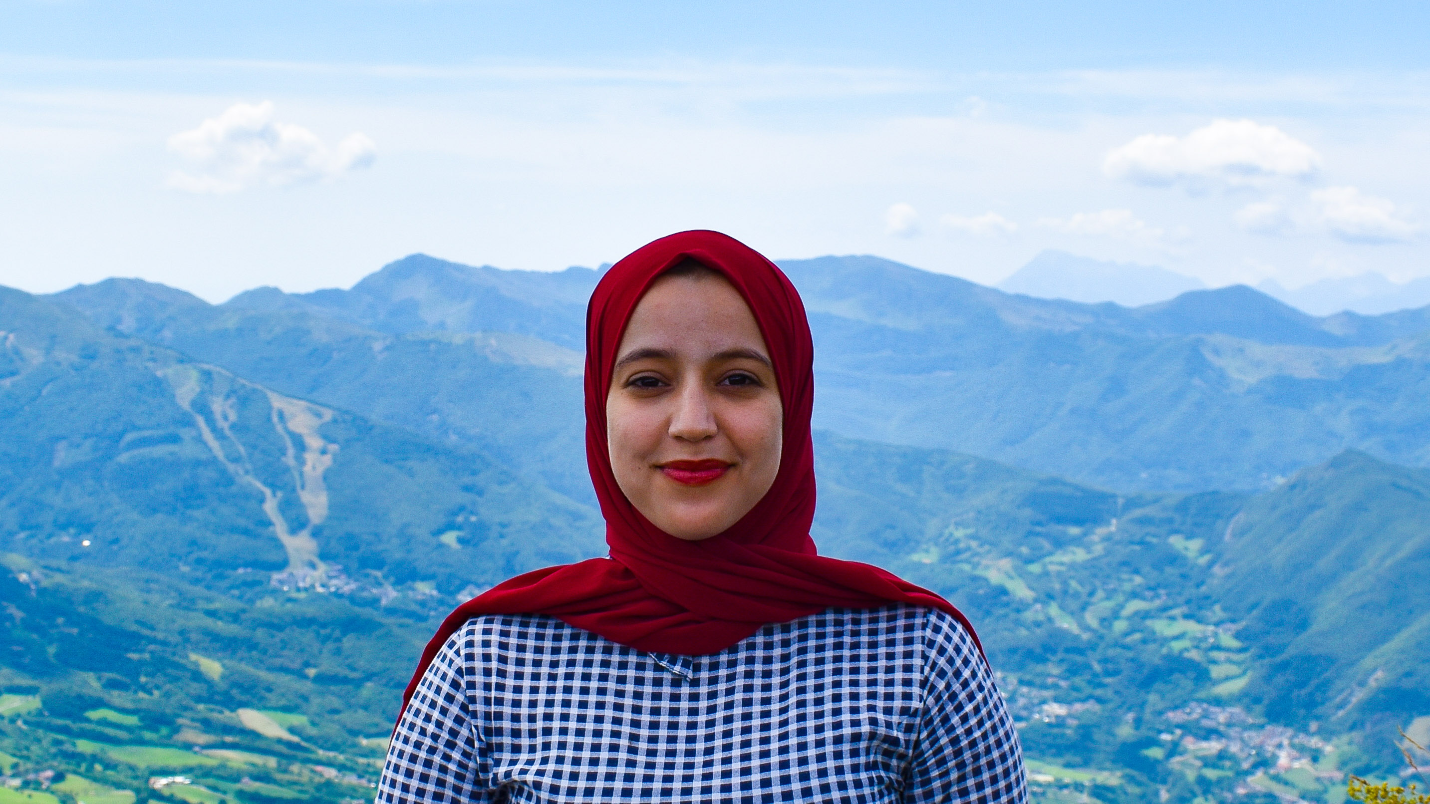 Imane Bou-Saboun, a PhD student in linguistics, standing on a mountaintop near her home in Italy, smiling at the camera
