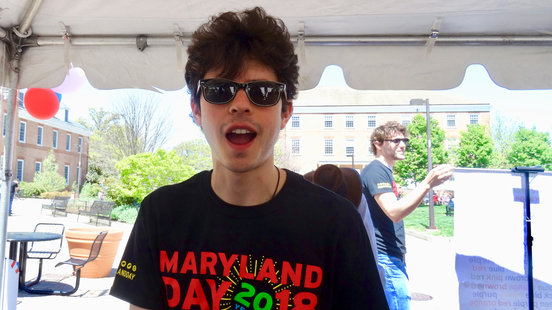 Rodrigo Ranero, a PhD student in Linguistics, wearing black sunglasses, wearing a Maryland Day t-shirt, looking at the camera with mouth open