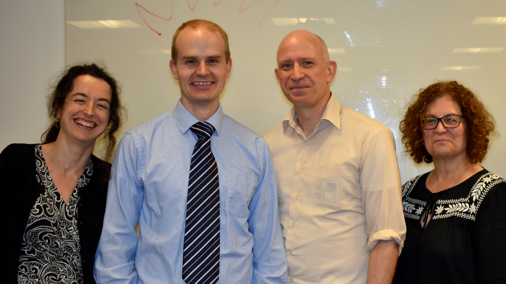 PhD student Jeffrey Green, wearing a tie, standing in front of a whiteboard with three members of his dissertation committee, 
