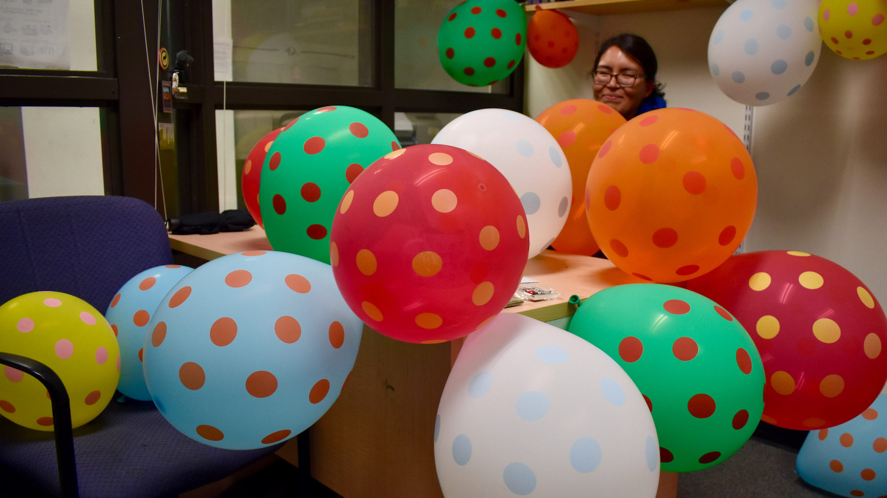 A table covered with polka-dotted balloons in different colors, and just barely visible through them: the smiling face of PhD student Sigwan Thivierge