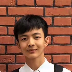A portrait of PhD student Jack Yuanfan Ying, seen from the shoulders up, standing in front of a brick wall, the backpack straps of a student visible on top of a white collared shirt