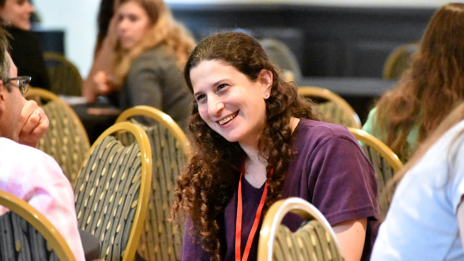Professor Naomi Feldman, seated in three-quarter profile, looking leftwards towards an unseen partner in conversation, and laughing with focussed eyes