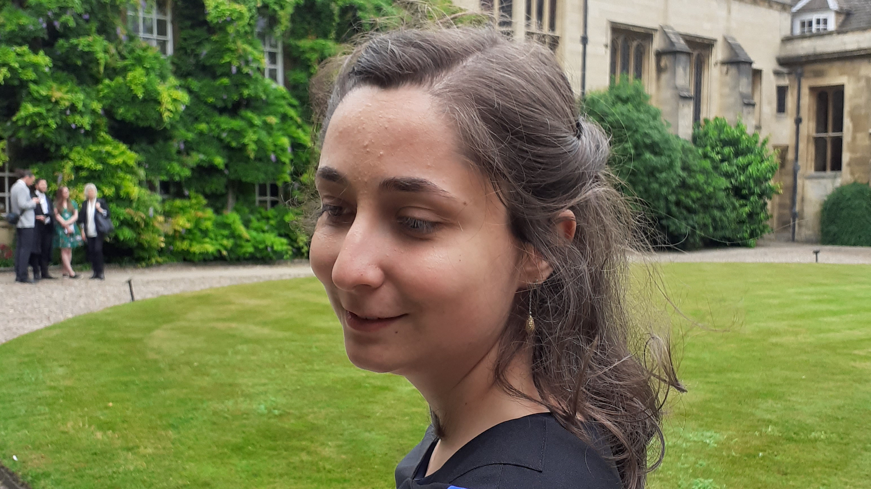 PhD student Clara Cuonzo, in profile, graduation robe just visible on her shoulders, standing on a green field of grass at Cambridge University