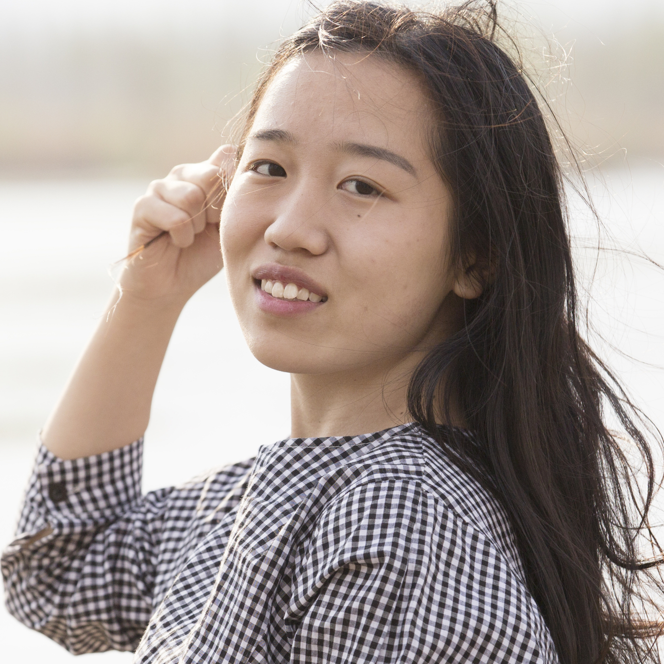 A portrait of PhD student Leslie Li, in three-quarter profile, right hand raised to her cheek, wind blowing