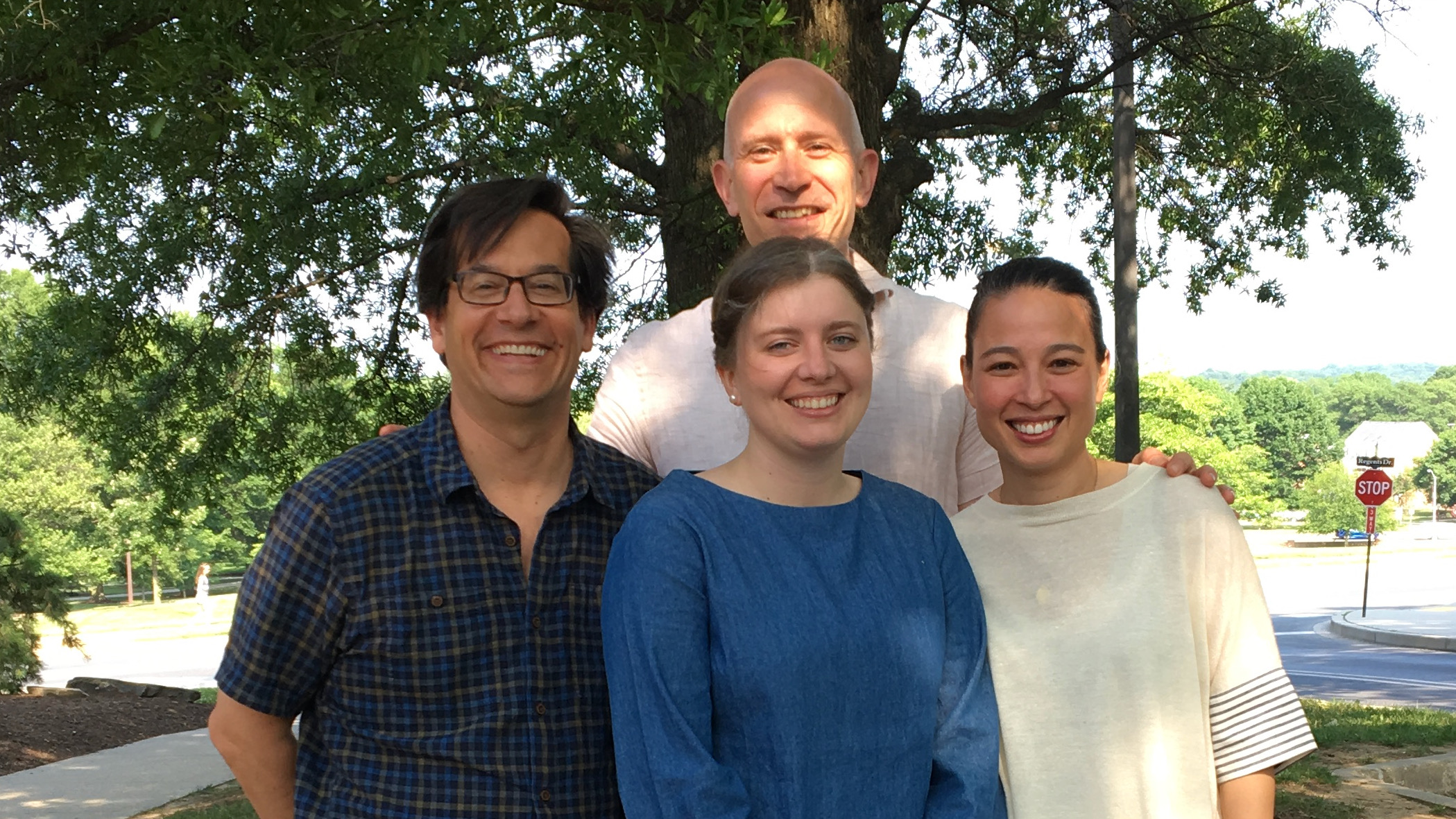 PhD student Rachel Dudley, flanked by her three PhD advisors, standing outside in the sun, smiling after a successful PhD defense.