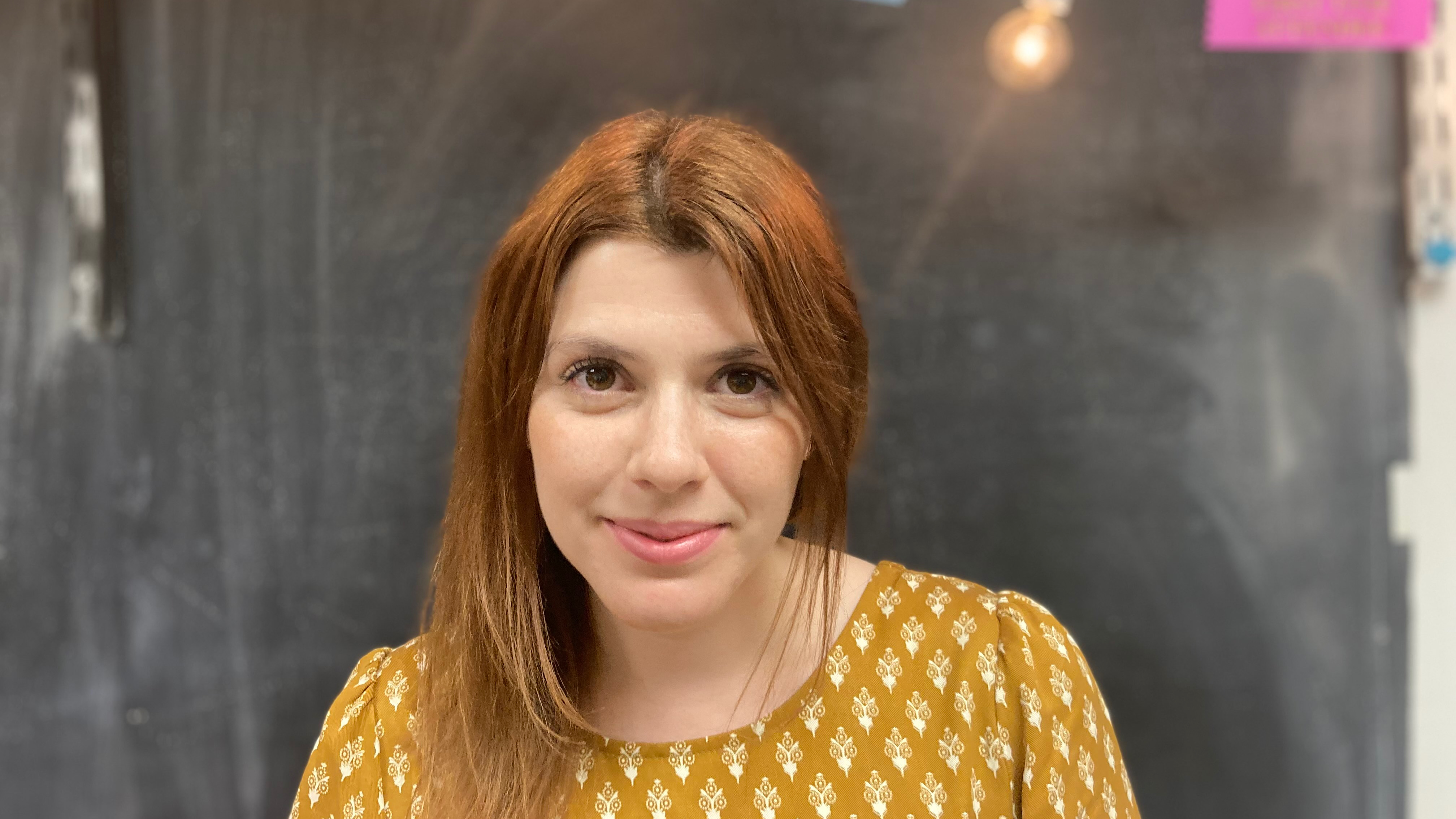 Linguistics PhD student Katherine Howitt, standing in front of a chalkboard, smiling at the camera.