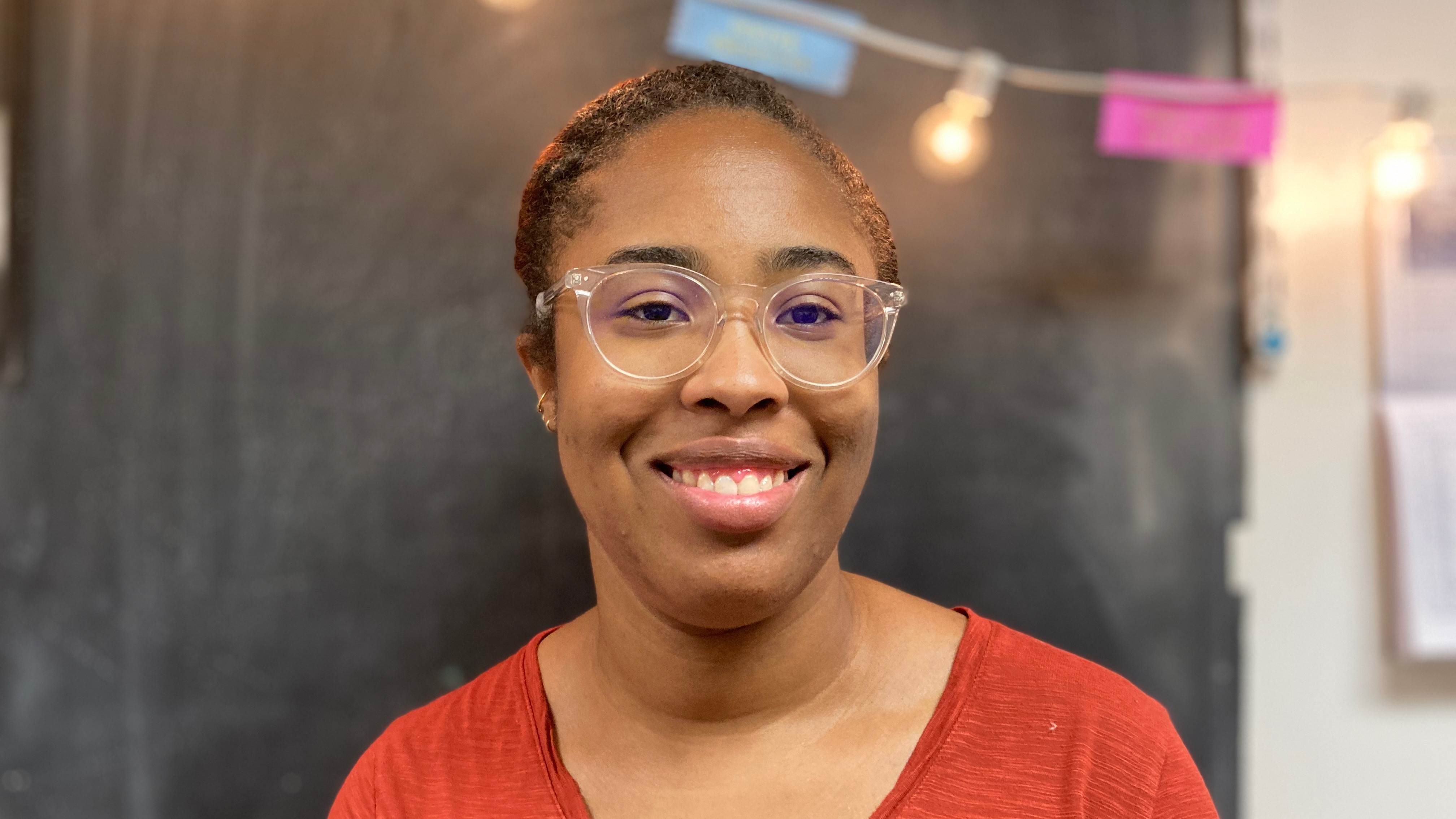 Linguistics PhD student, London Dixon, standing in front of a chalkboard and smiling