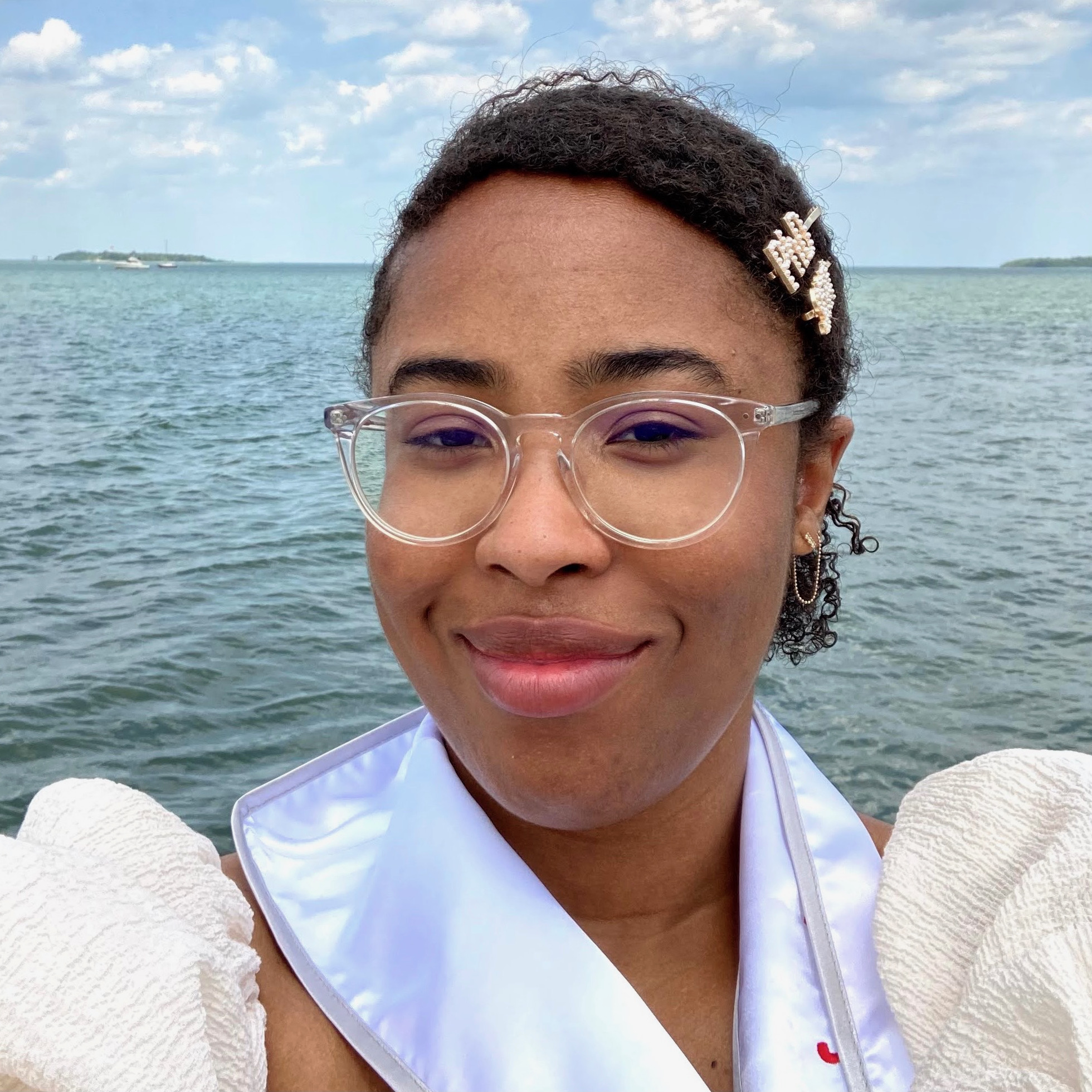 Linguistics PhD student, London Dixon, smiling at the camera, with a calm ocean behind her, and a barrette in her hair that says "PhD"..