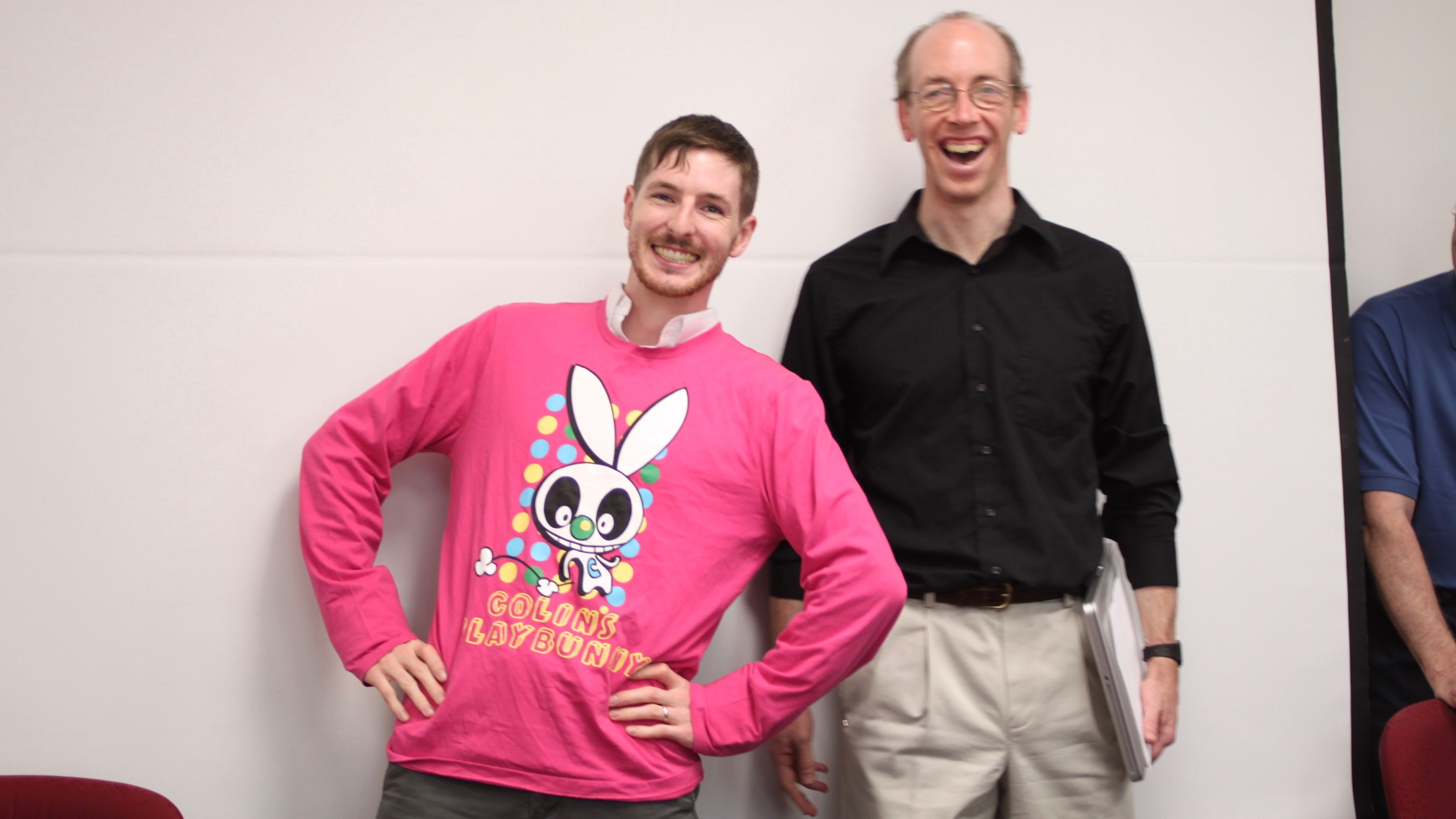 PhD student Brian Dillon in a pink long-sleeve jersey that says "Colin's Plaything", arms akimbo and smiling comically, standing next to his advisor Colin Phillips, who is erupting with laughter.
