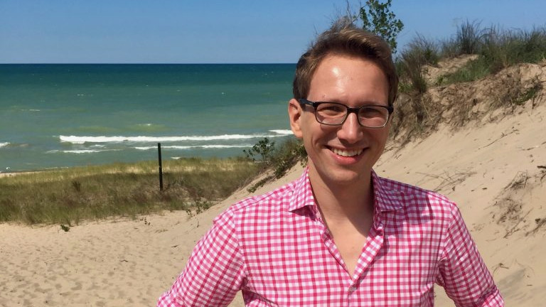 University of Chicago Professor of Philosophy, Malte Willer, standing on a lakeshore beach, smiling