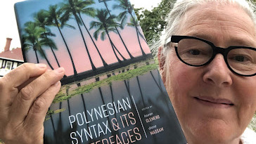 A close-up shot of an older woman holding up a book called "Polynesian Syntax and its Interfaces," with a cover photo of palm trees filtering a setting tropical sun.