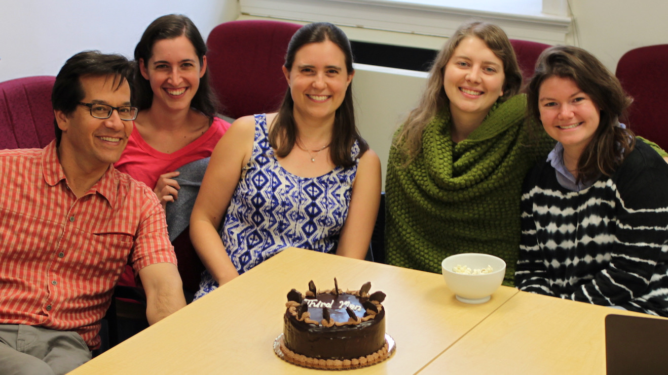 Five people sitting around a chocolate cake.