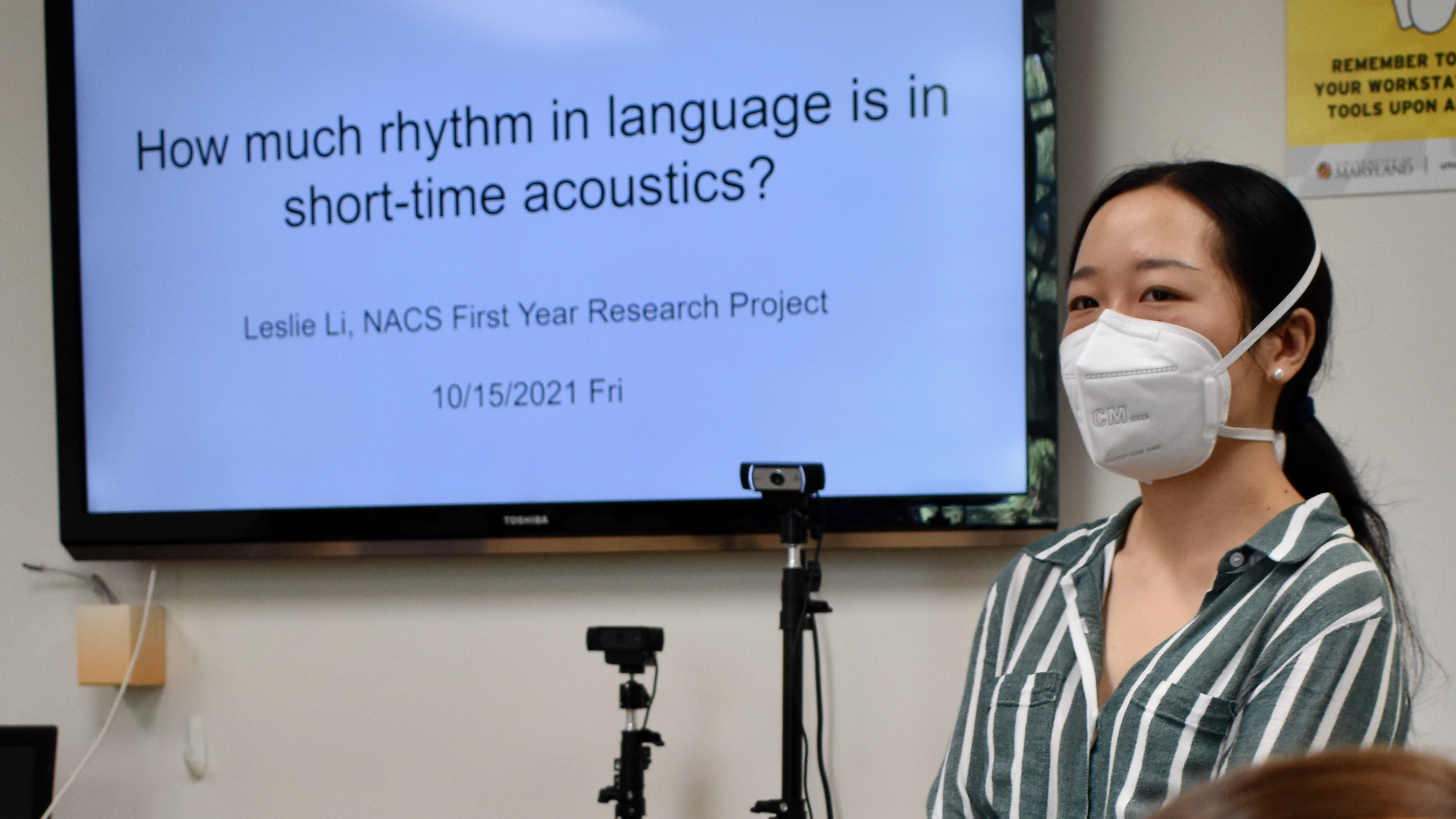 PhD student Leslie Ruolan Li, in three-quarter profile, standing in front of TV screen projecting the title of her presentation, "How much rhythm is in short-time acoustics?"