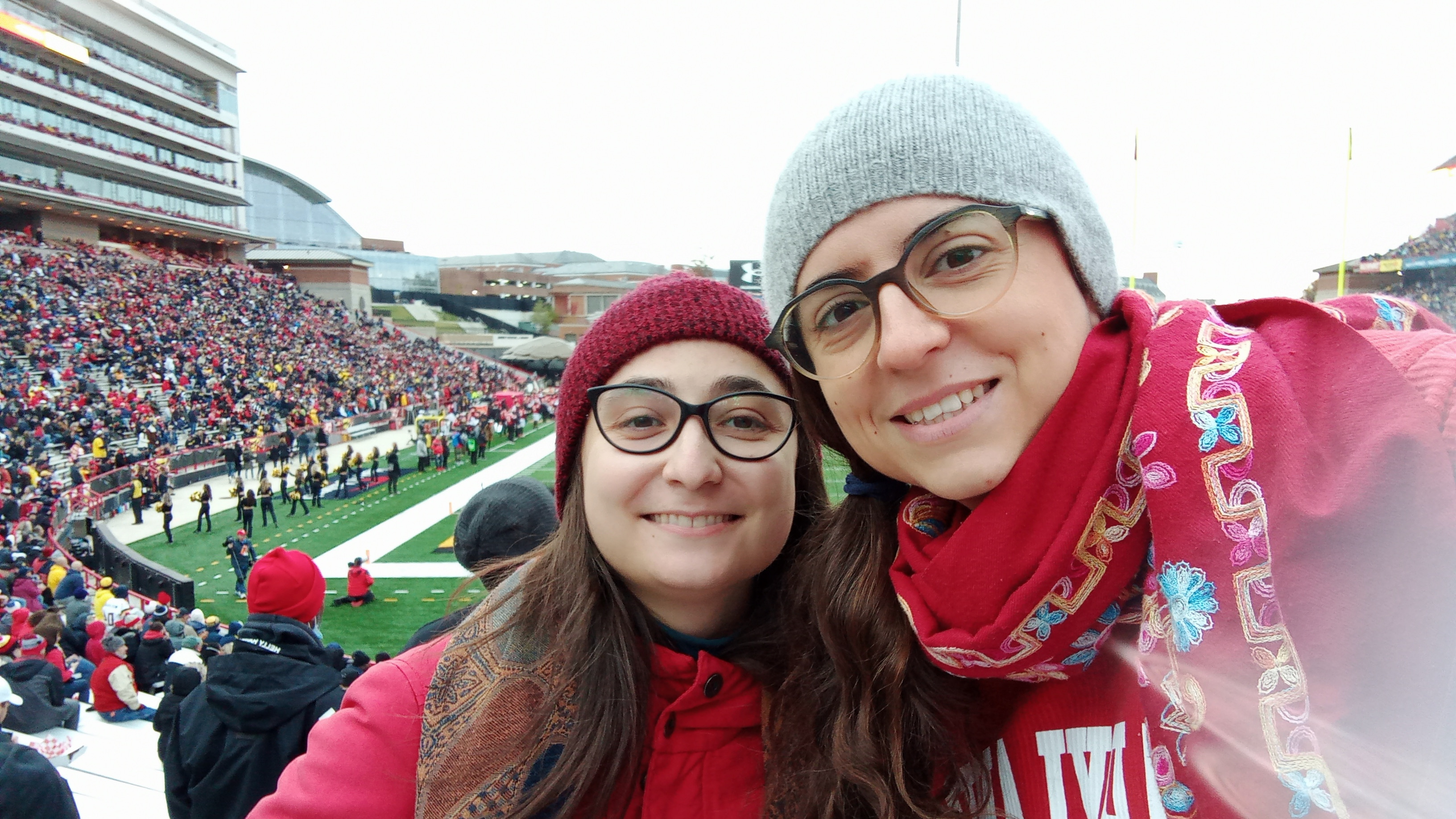 Clara Cuonzo and Luisa Seguin, two PhD students in Linguistics, taking a joint selfie at their first football game, both wearing read, standing behind the endzone at the Maryland stadium,