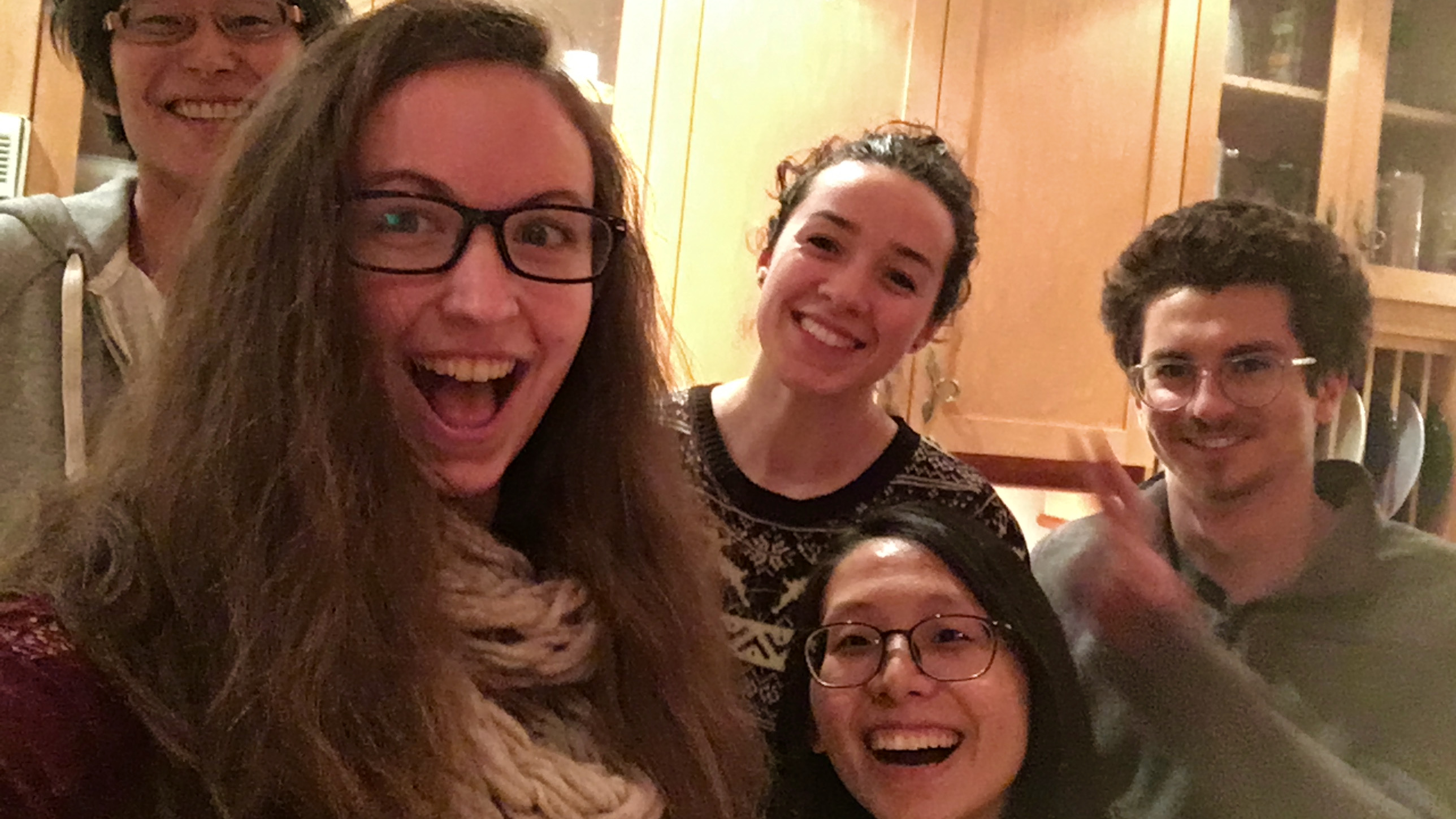 A selfie in a kitchen in the evening, showing five graduate students smiling and laughing at the camera.