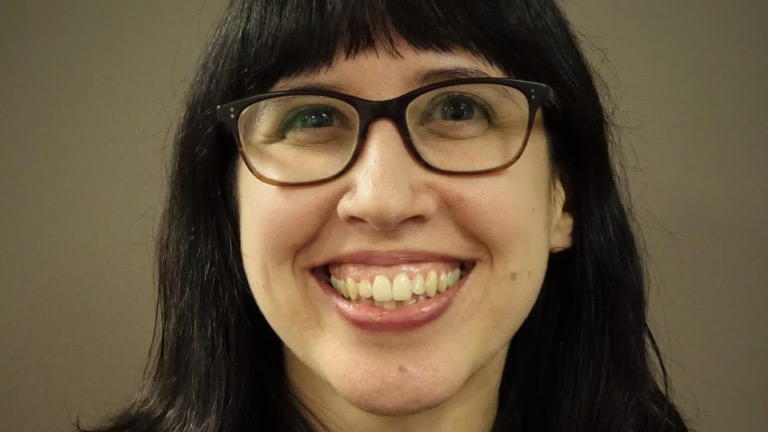 Close portrait of a young woman with dark hair and dark glasses, smiling broadly