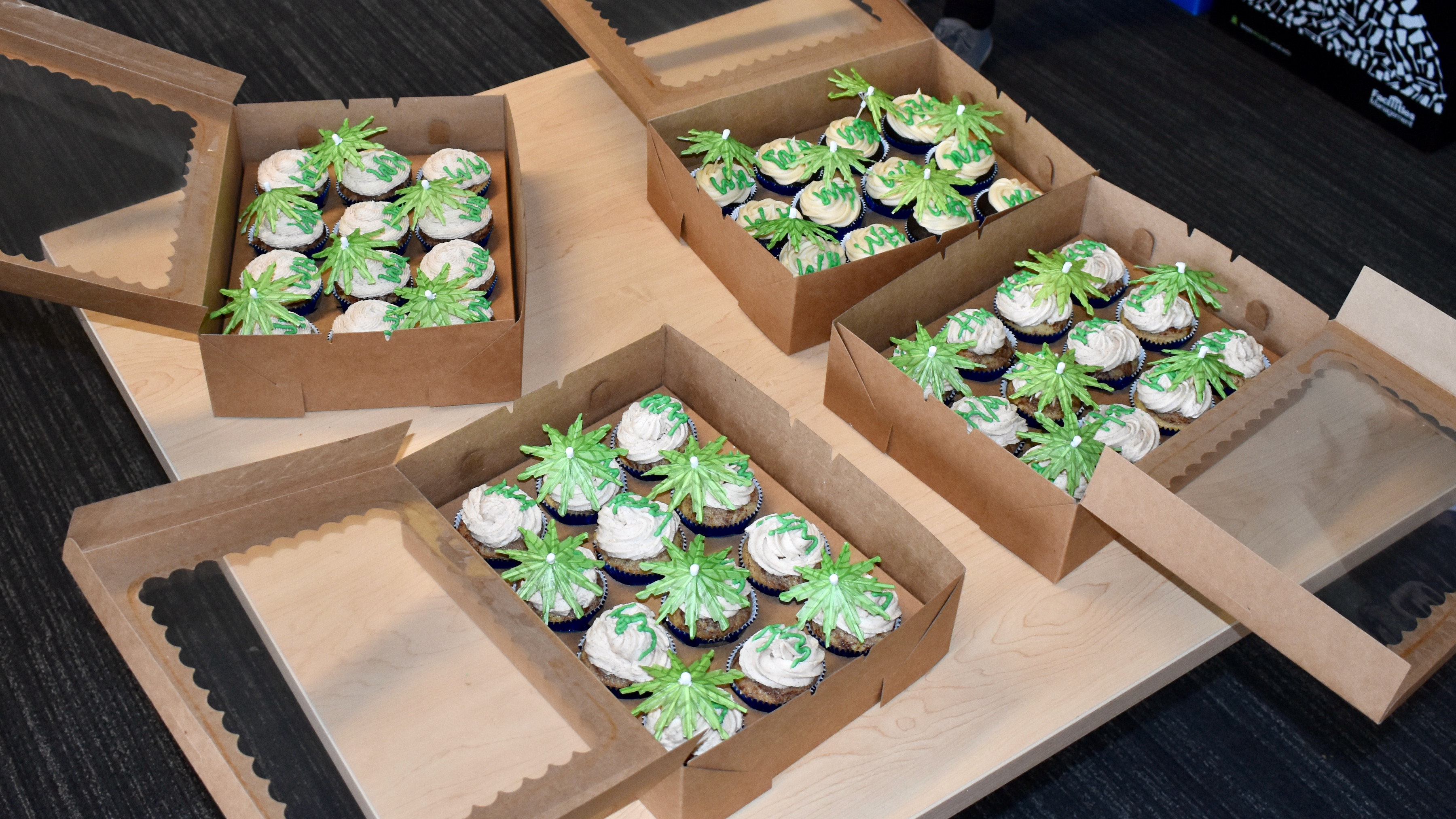 Four boxes of cupcakes with green frosting and palm tree cocktail umbrellas.