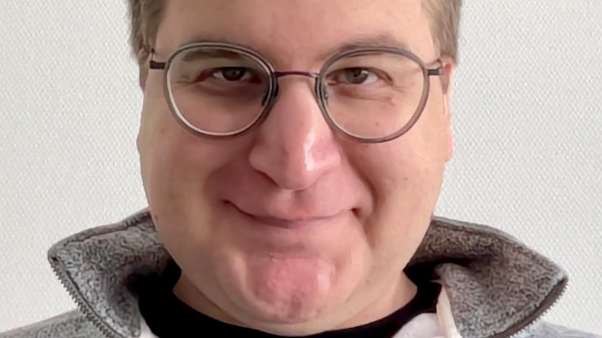 A close portrait of the smiling face of young man wearing glasses.