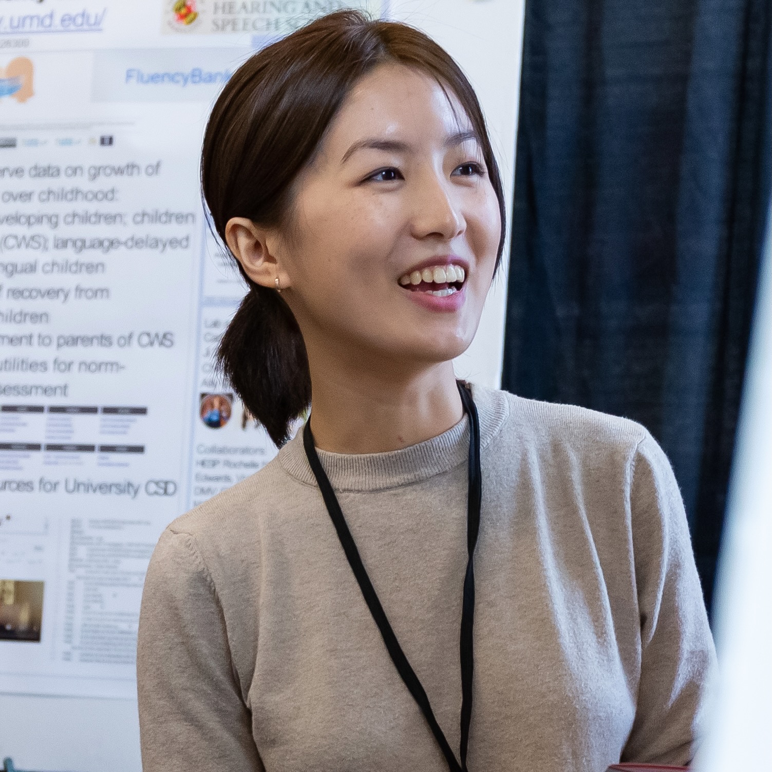 Photo of a young woman smiling broadly as she presents her research.