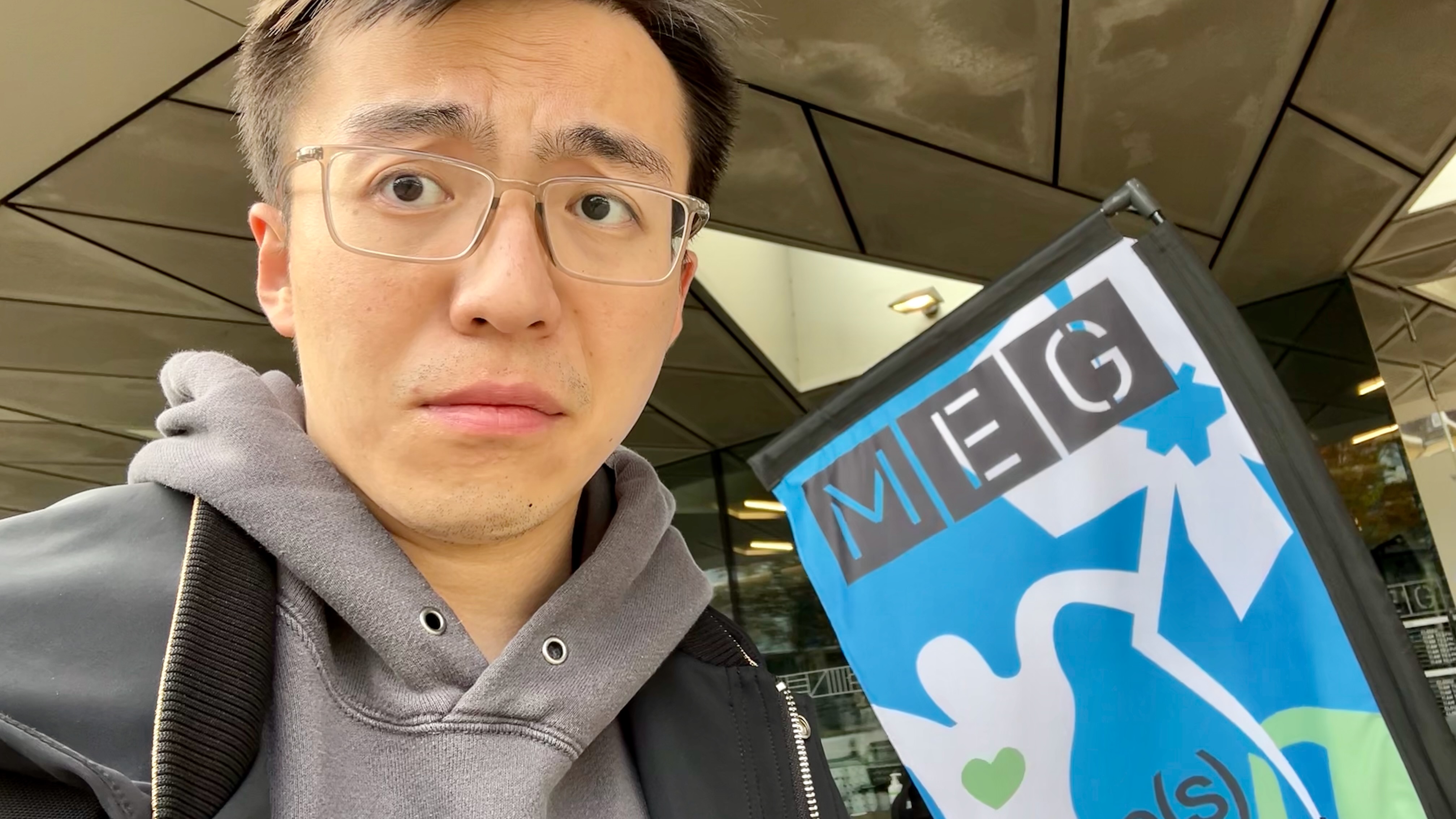 Selfie in front of young man looking theatrically quizzical, in front of a sign that says "MEG".