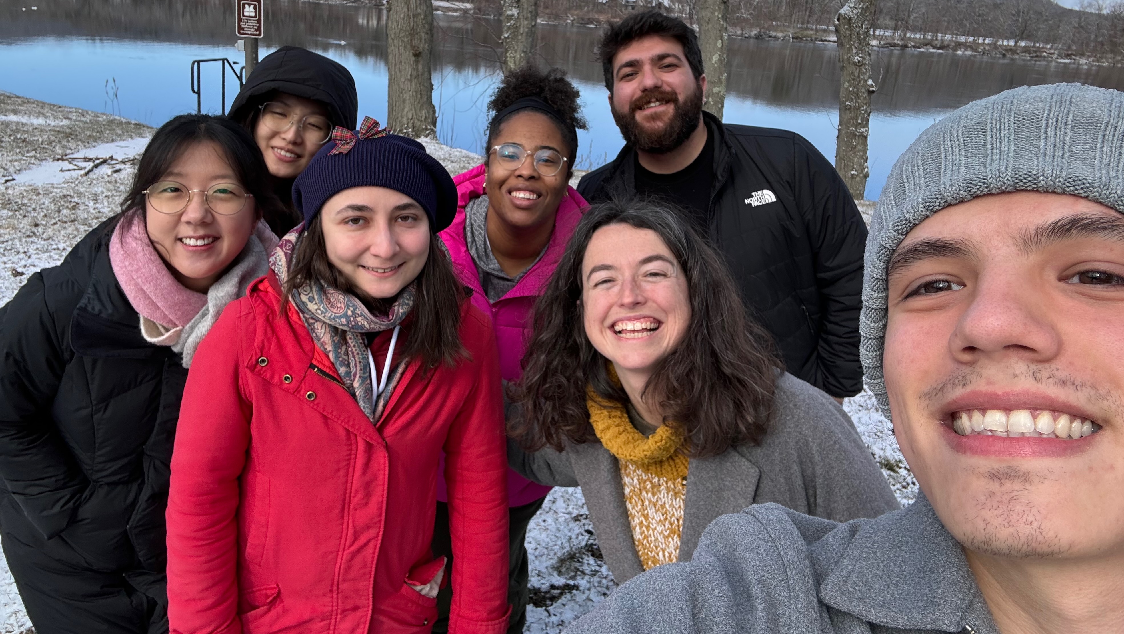 Selfie of a group of graduate students outdoors during the winter, standing in front of a frozen pond.