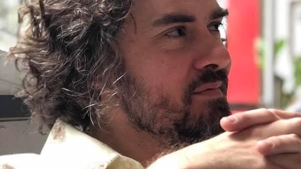 Close profile portrait of a man with wavy brown hair and a short beard.