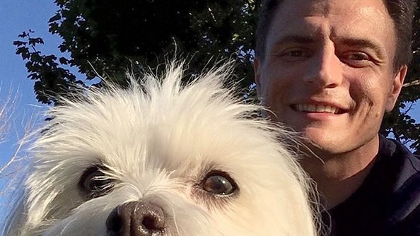 Close photo of the snout and eyes of a fluffy white terrier, with a man's face behind.