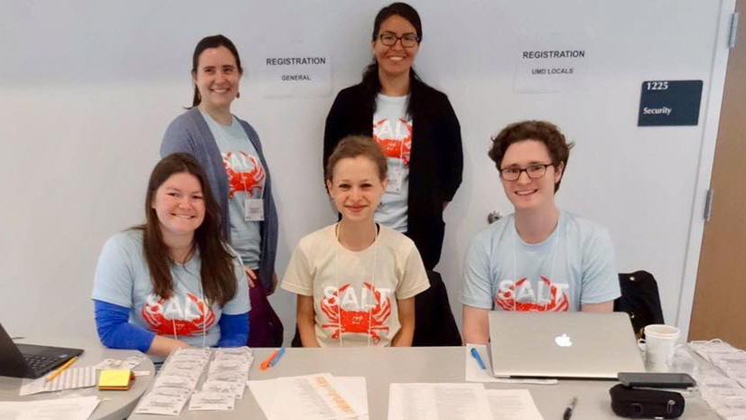 Five young people in matching t-shirts, sitting at a registration table.
