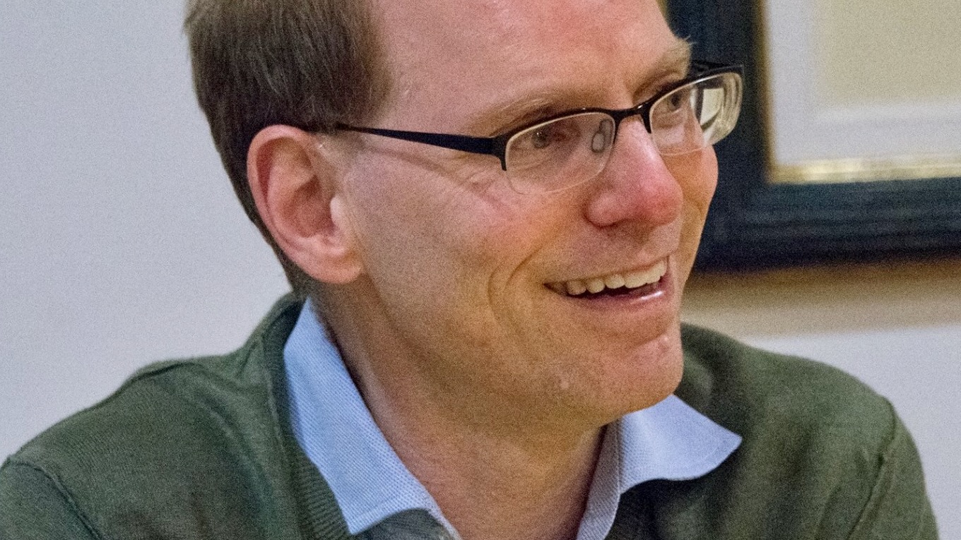 Close portrait of a man's face in three-quarter profile, wearing glasses, about to talk through a half smile.