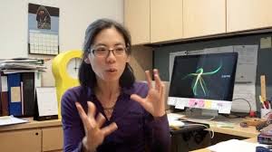 A professor at her desk, computer in the background, talking animatedly.