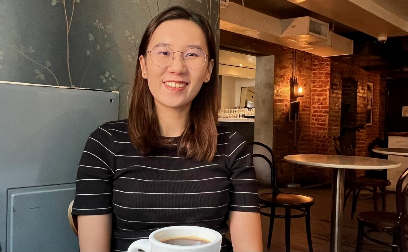 A cheerful young woman in a cafe, smiling at the camera.