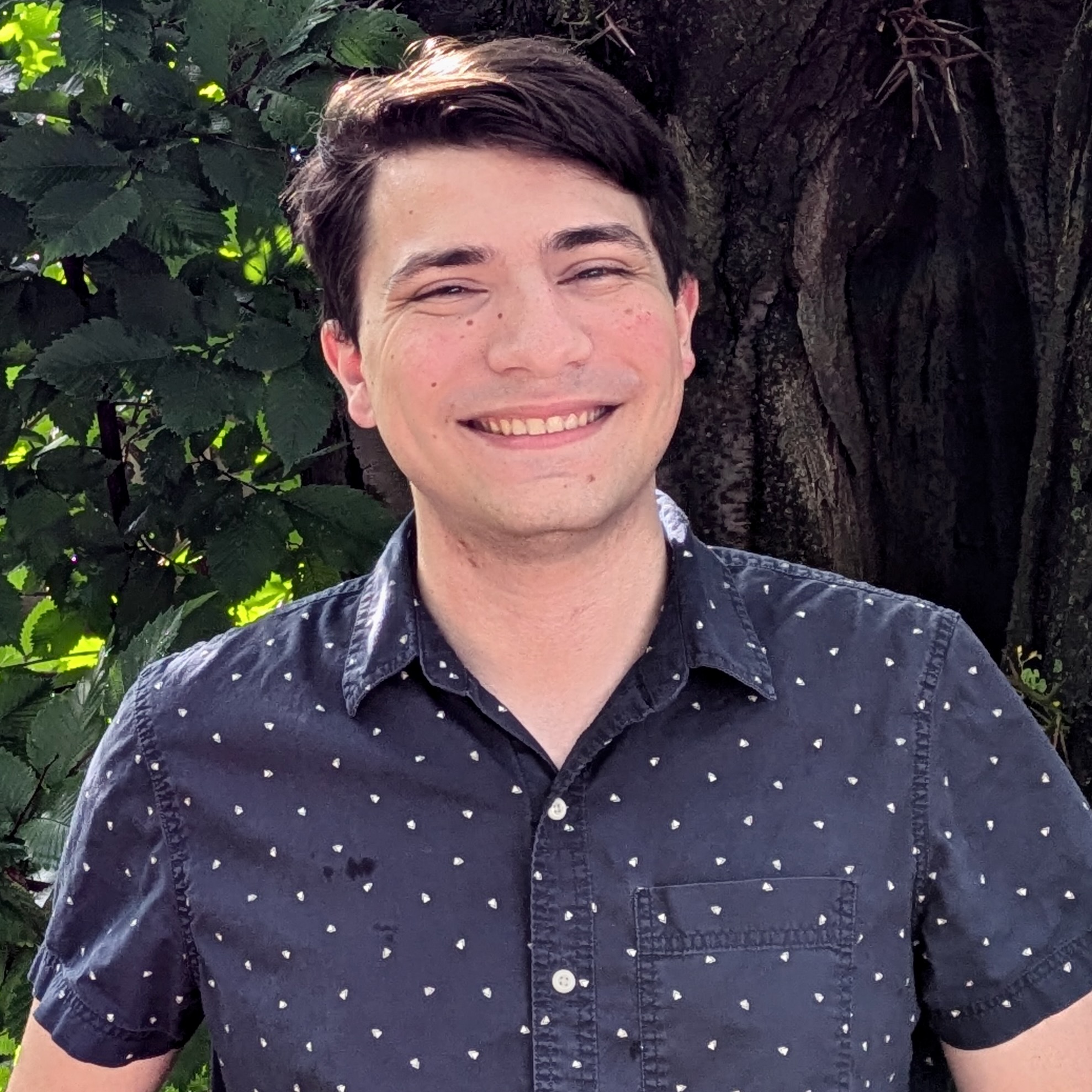 A young man, standing outside, smiling.