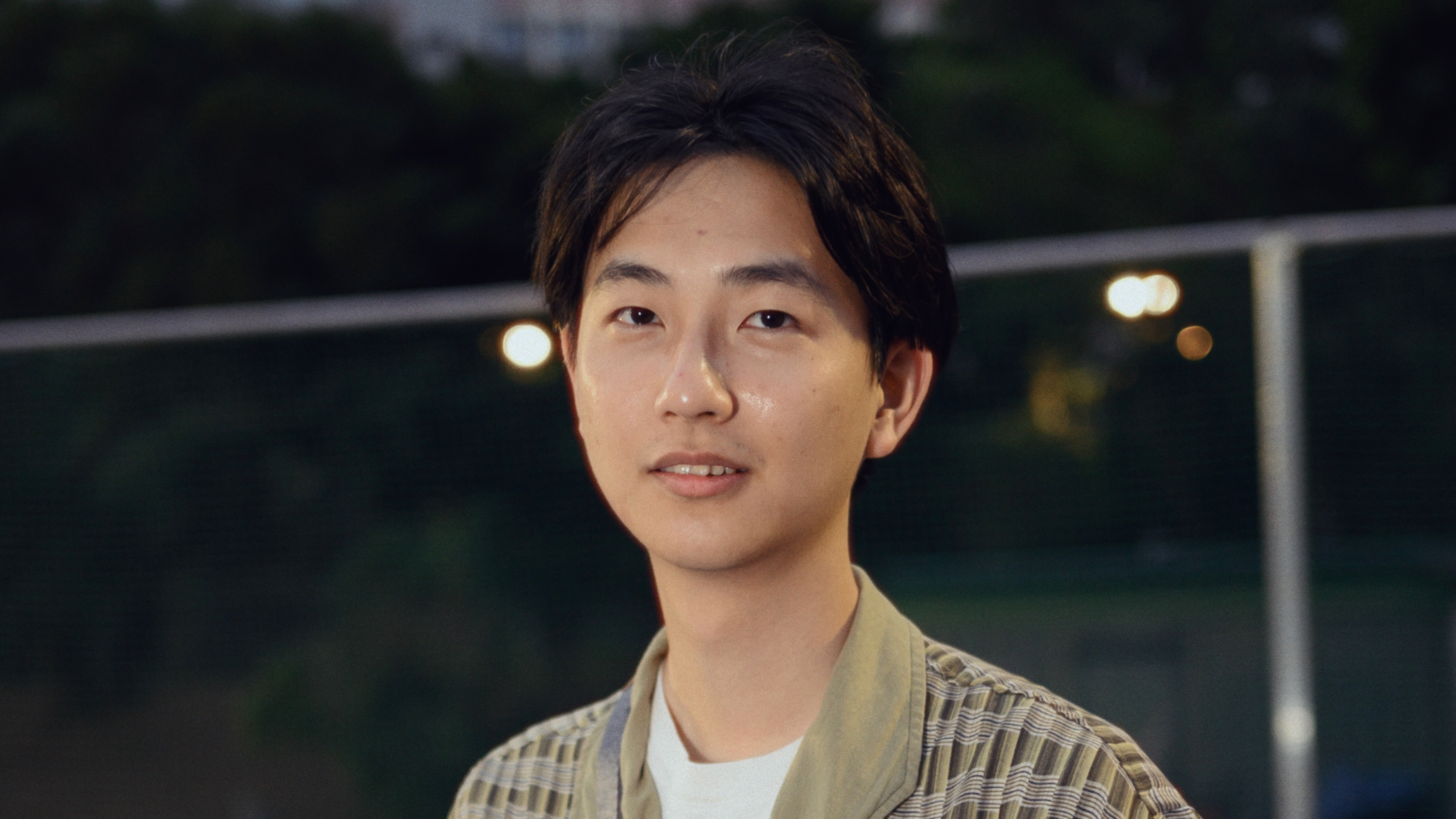 A young man, standing outside at nighttime, looking calmly at the camera.