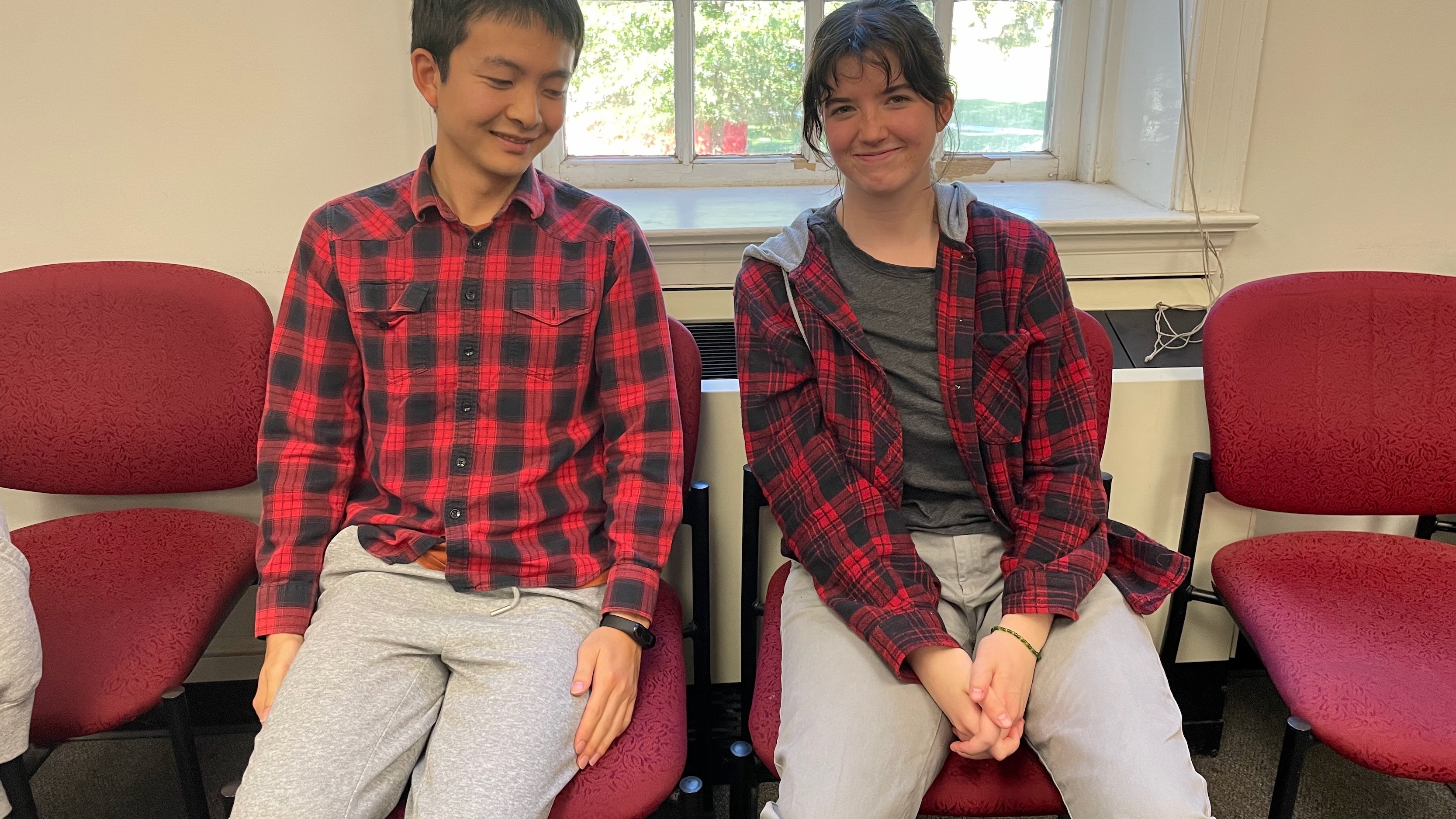 A young man and a young woman, both in red-and-black lumberjack shirts and grey sweatpants.