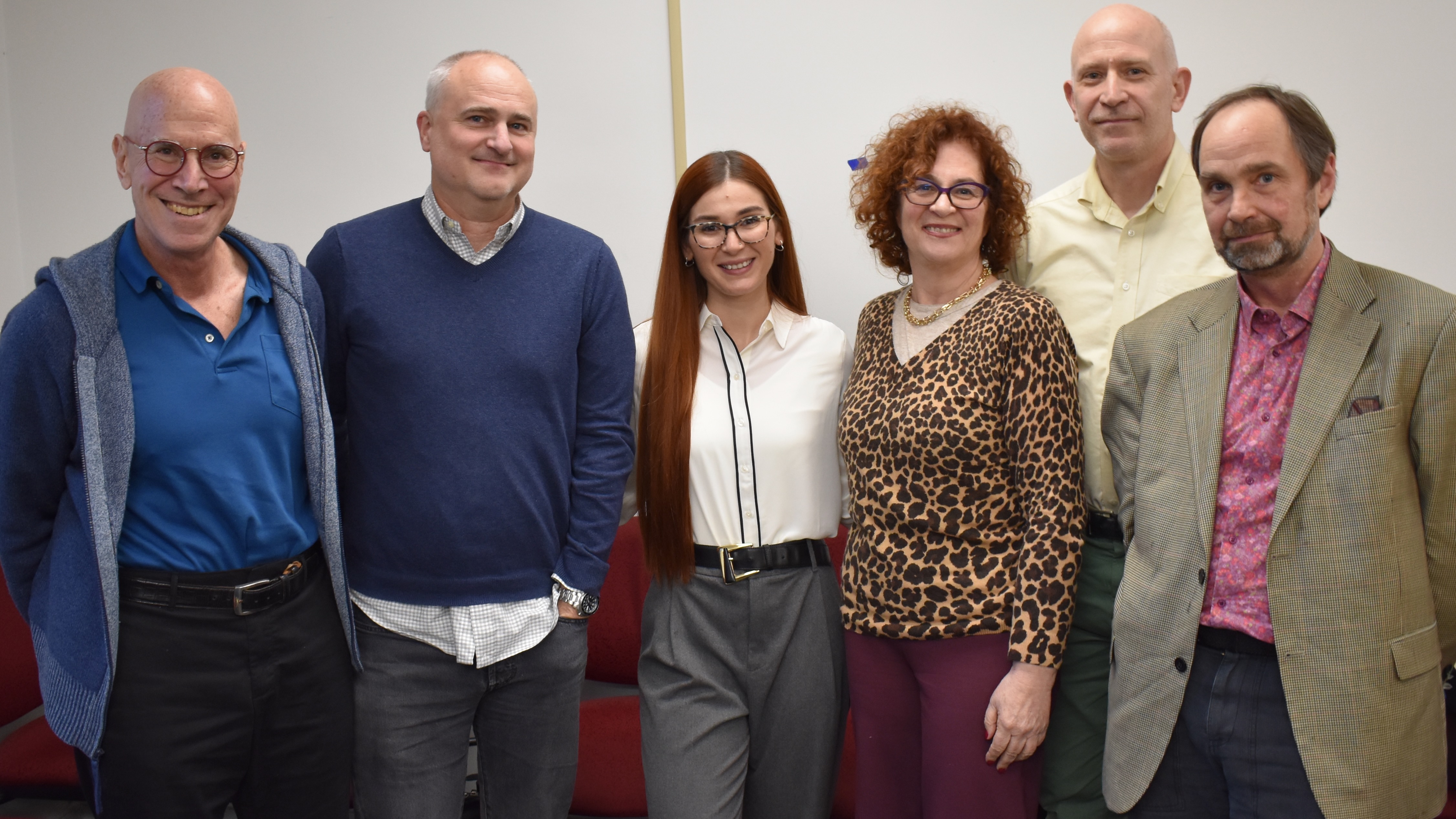 Six people, standing in a line, posing for a formal portrait: it's a dissertation student, having just successfully defended her dissertation, flanked by her examining committee.