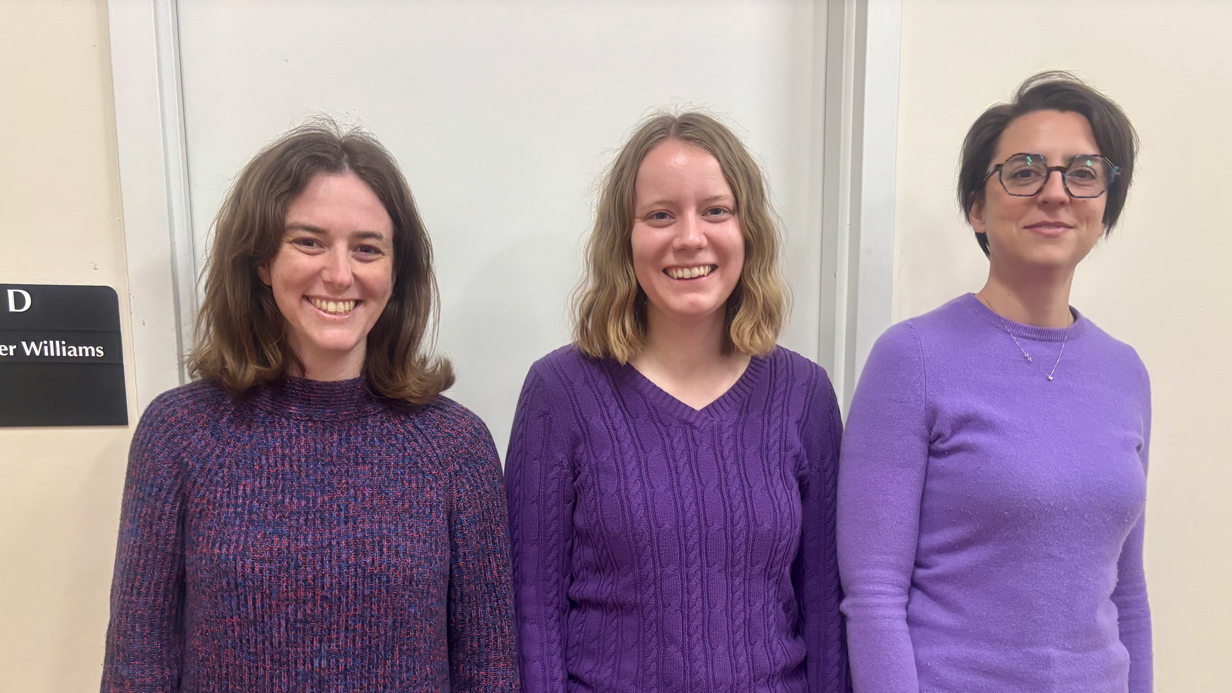 Three young women, all wearing purple sweaters.