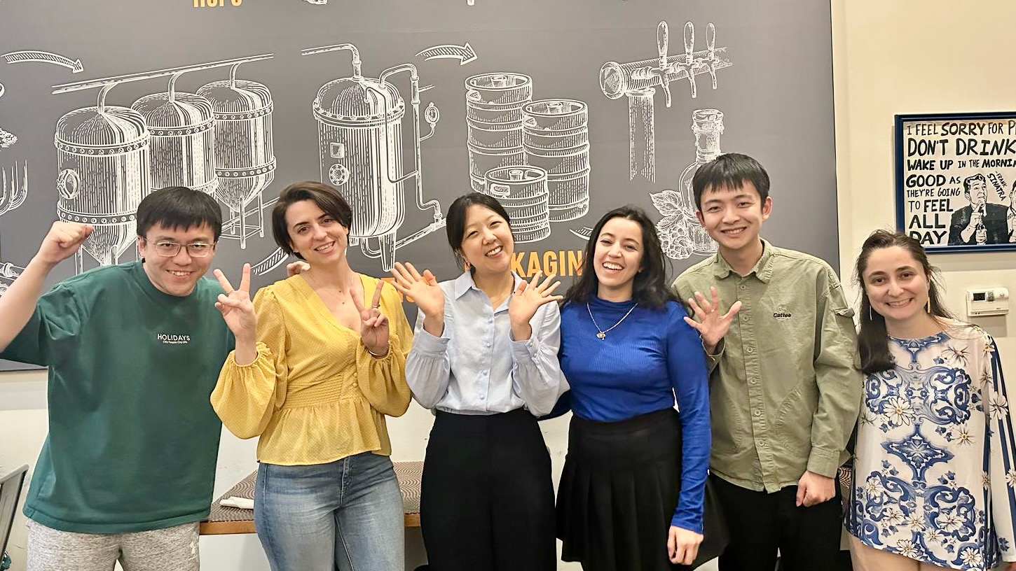 Six young people standing in a row, waving and smiling for a group photo.
