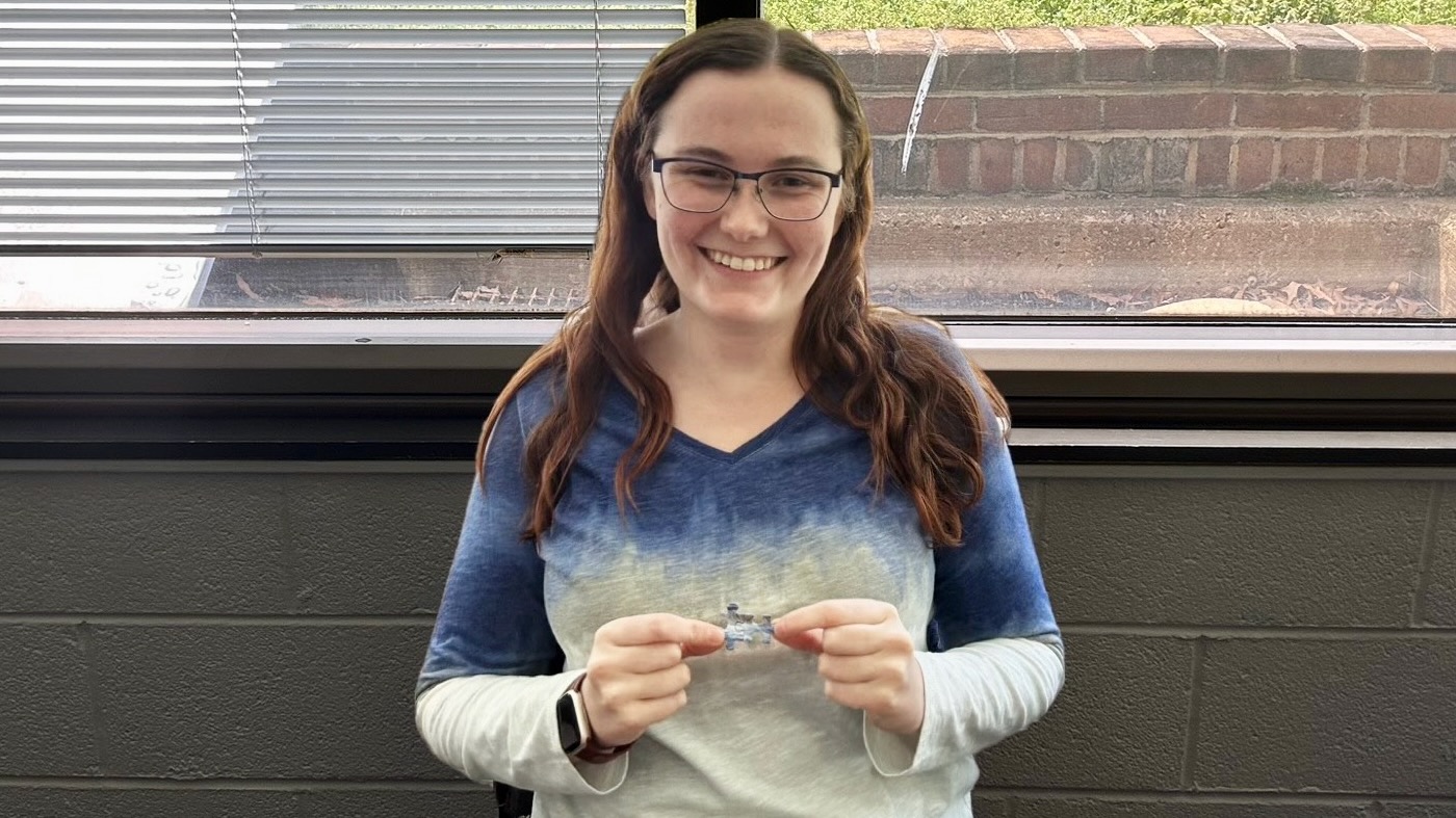 A woman holding up a single piece of a jigsaw puzzle, which happens to exactly match the top she is wearing.