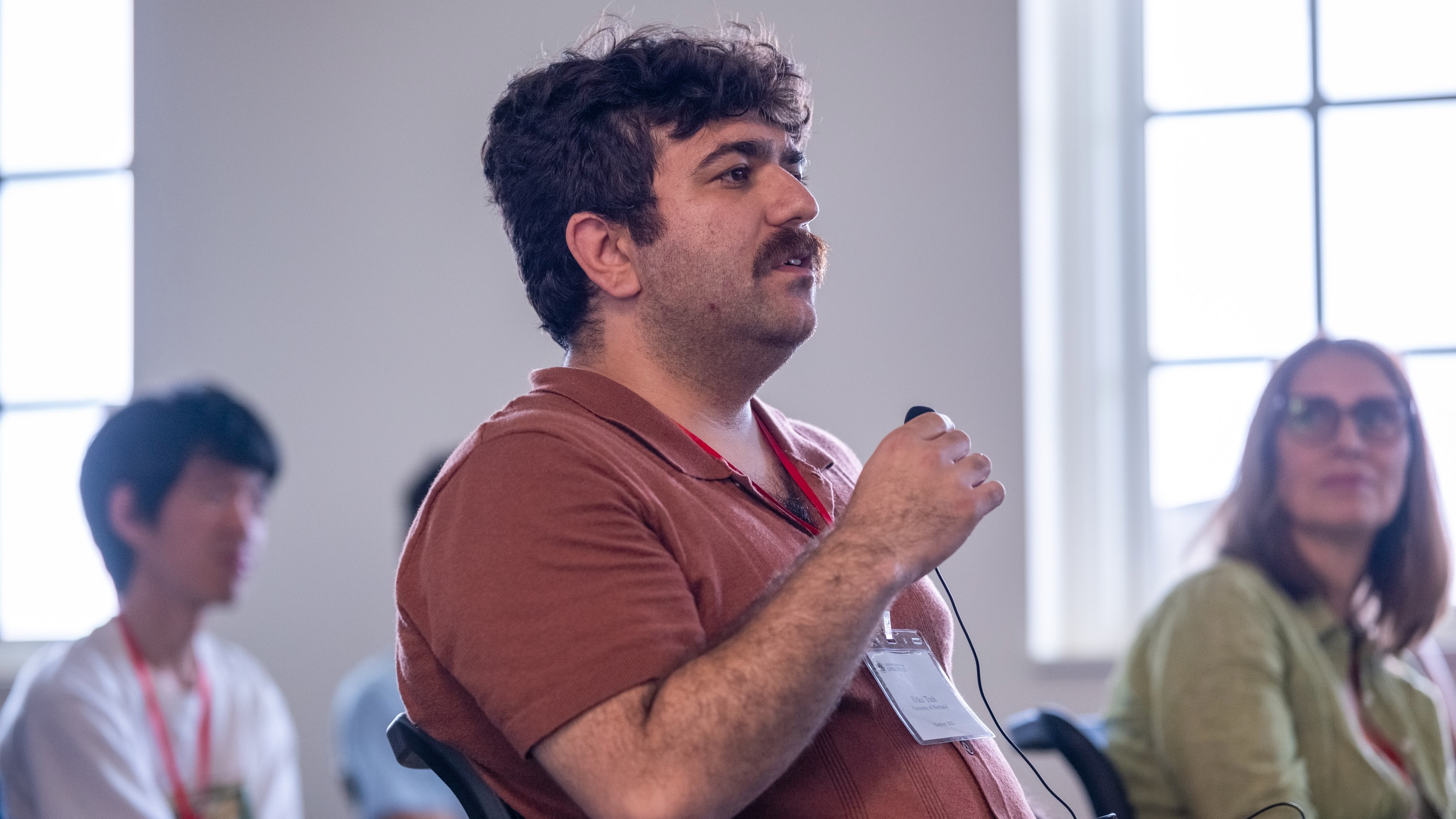 A young man with a mustache asking a question into a microphone.