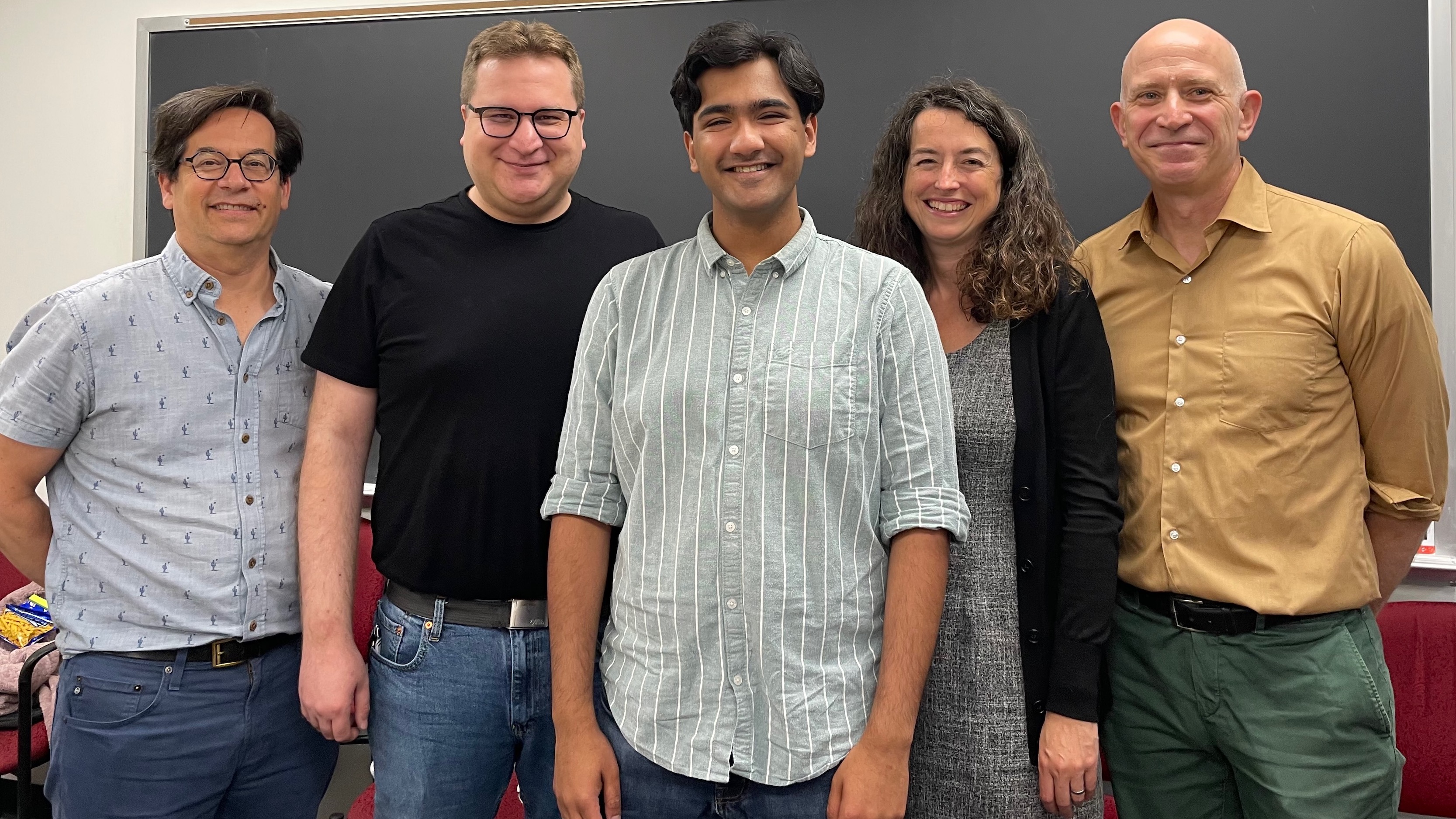 A young man flanked by the review committee for his qualifying paper. 