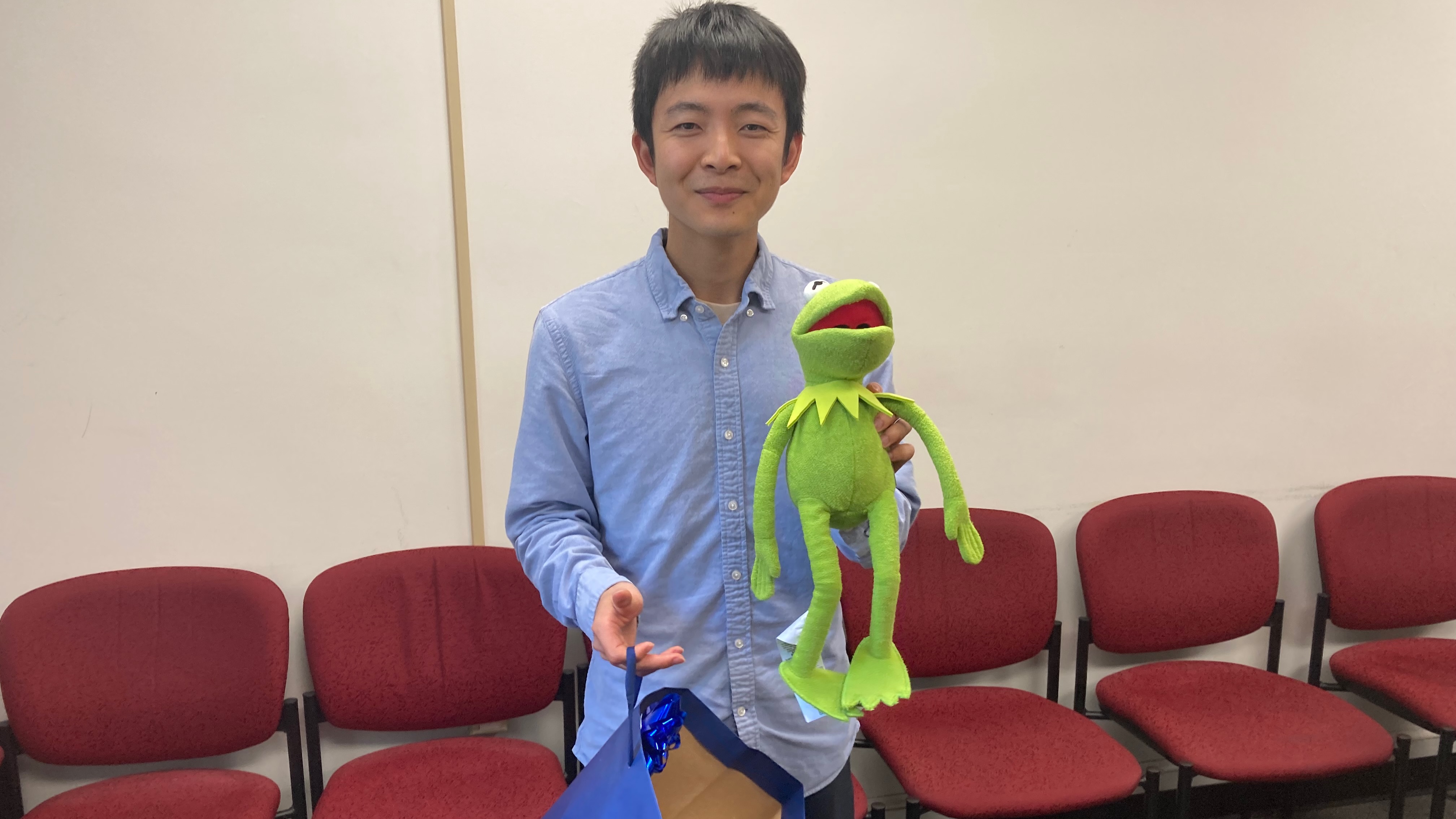 A young man holding a Kermit the Frog puppet.