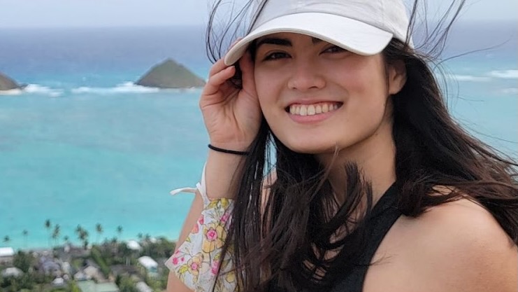 A young woman in a white baseball cap, with a turquoise tropical sea in the background.