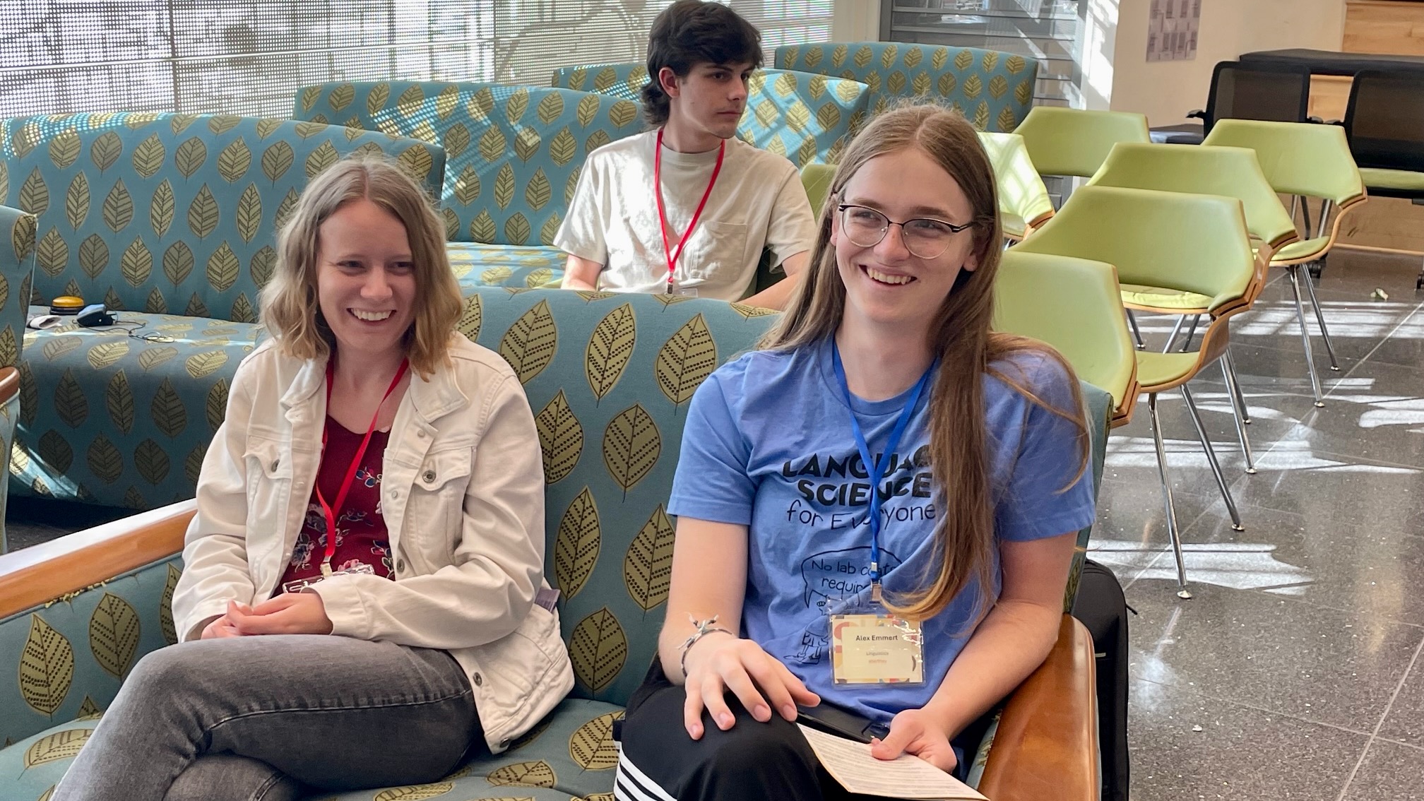 A young woman and a young man, both on a sofa in a room bathed in outdoor sunshine, laughing.