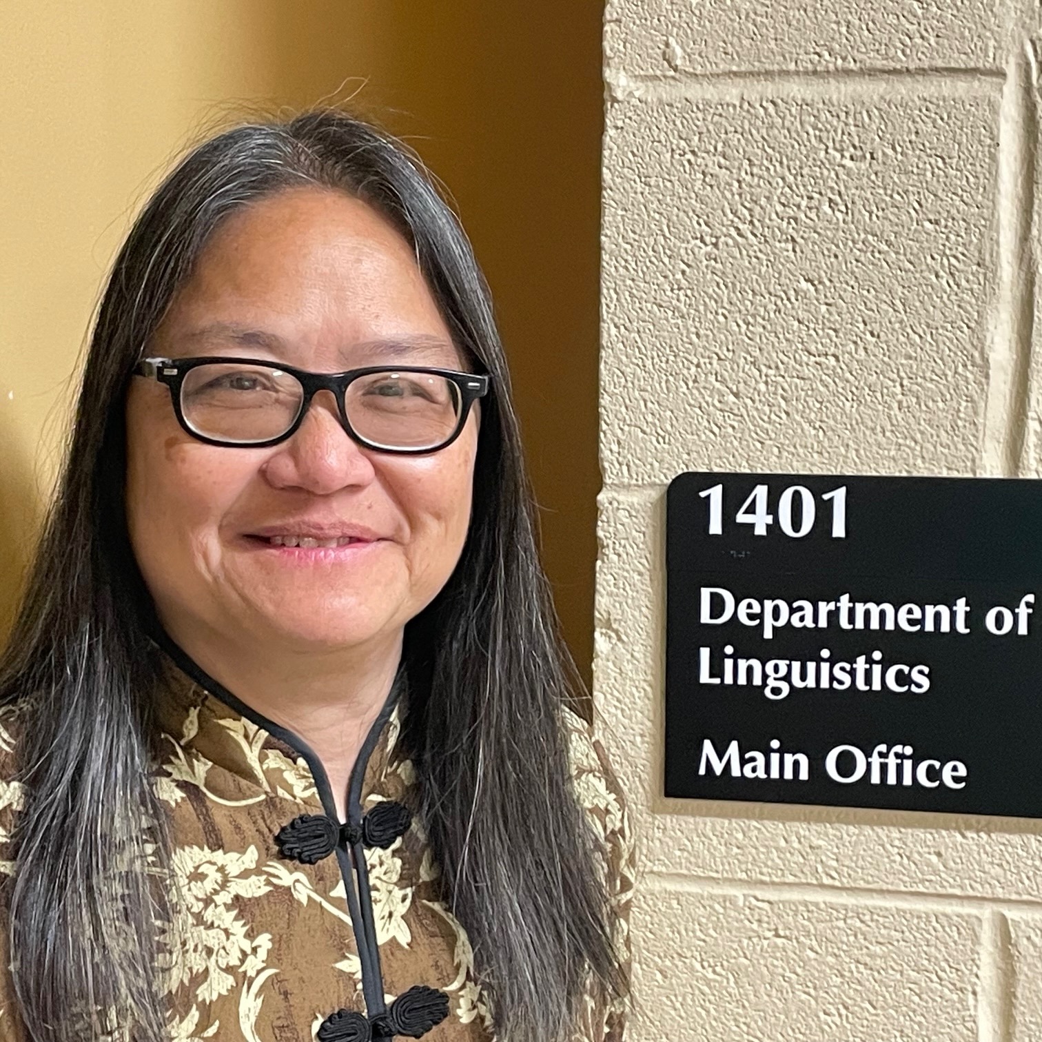 A woman smiling, standing next to the door of her office.