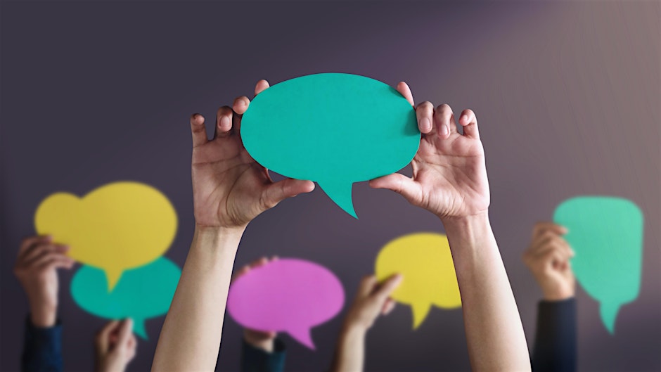 Multiple sets of hands holding up paper cutouts of speech bubbles in various colors.