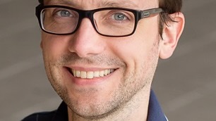 Professional headshot of a young man, smiling, wearing glasses.