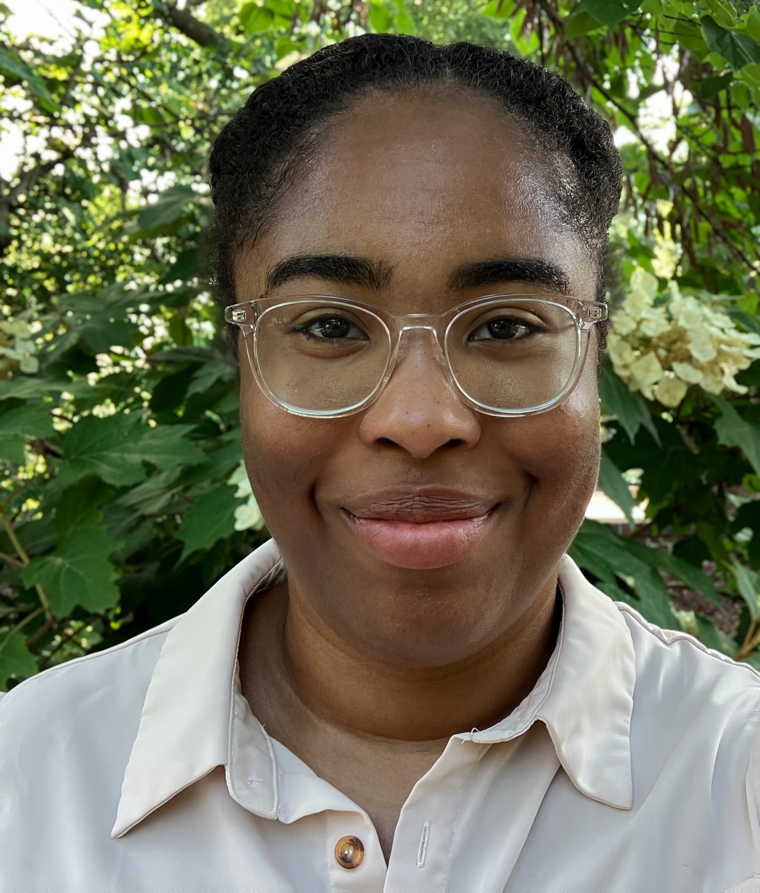A young woman smiling at the camera wearing a white button down and glasses
