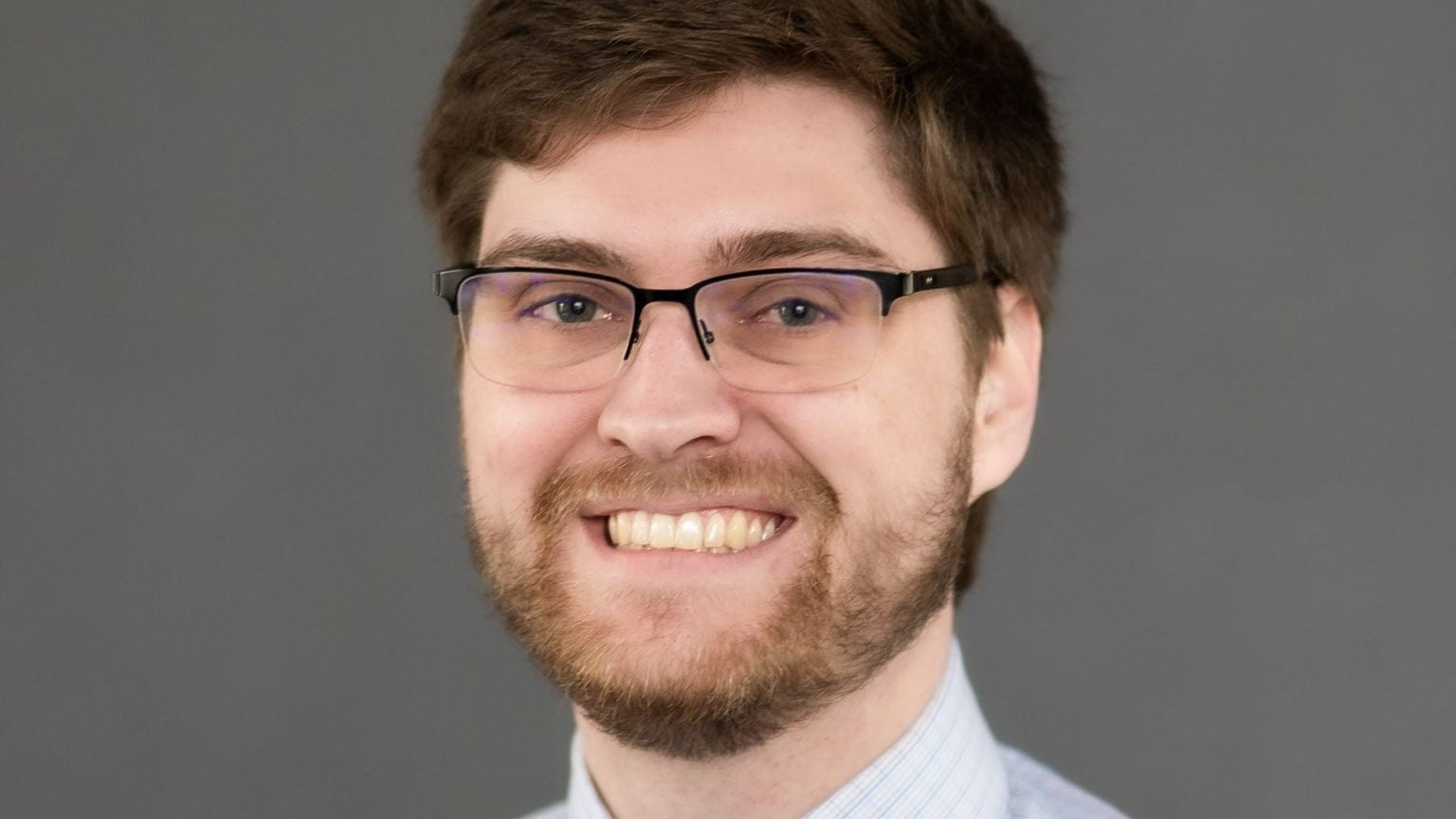 Professional headshot of a young man, beard and glasses.