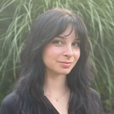 Portrait of a young woman in three-quarter profile, standing in front of tall grasses.